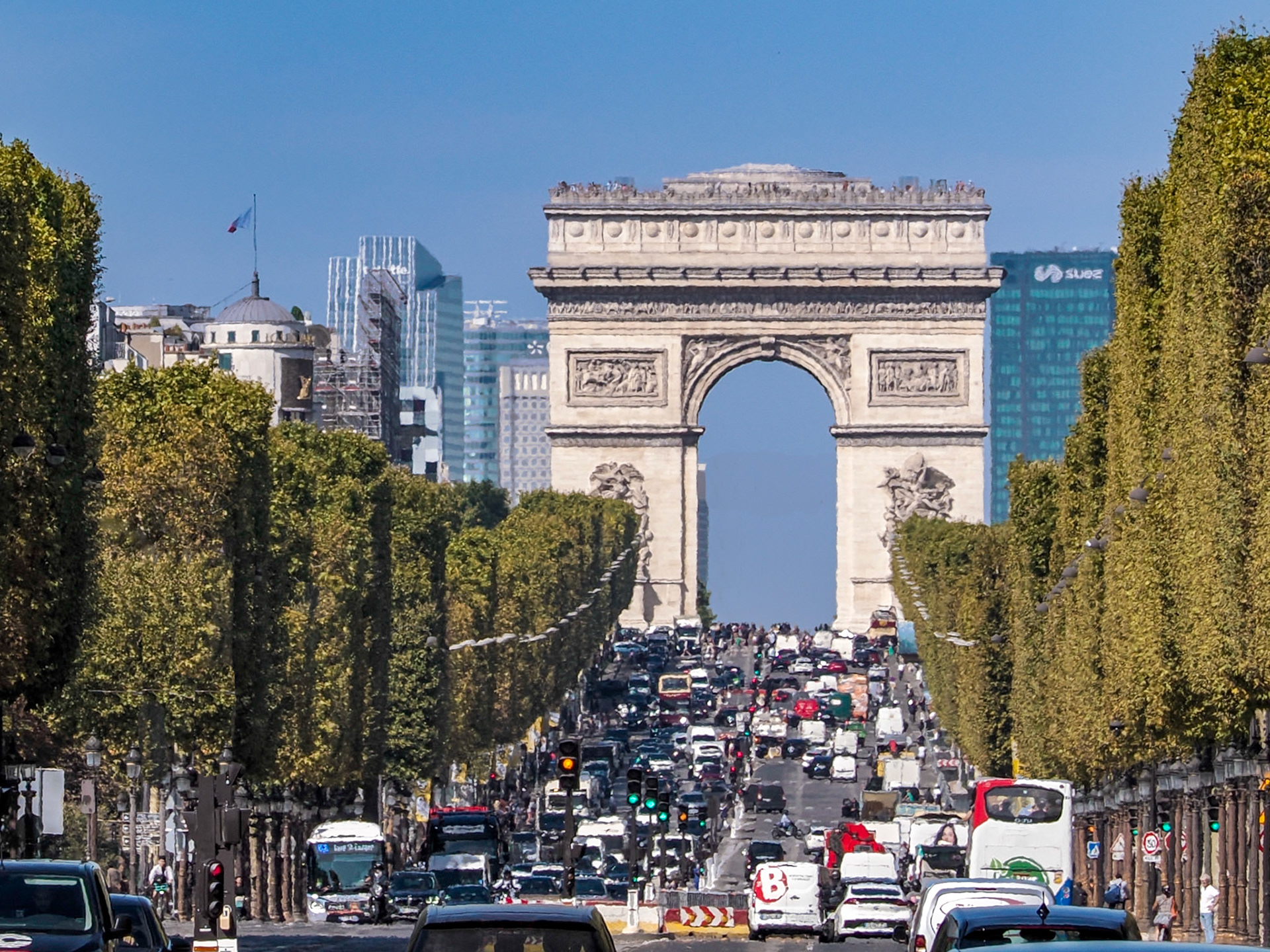 The Arc de Triomphe and traffic on the busy Champs-Élysées, lined with London plane trees, shimmer in the summer heat.