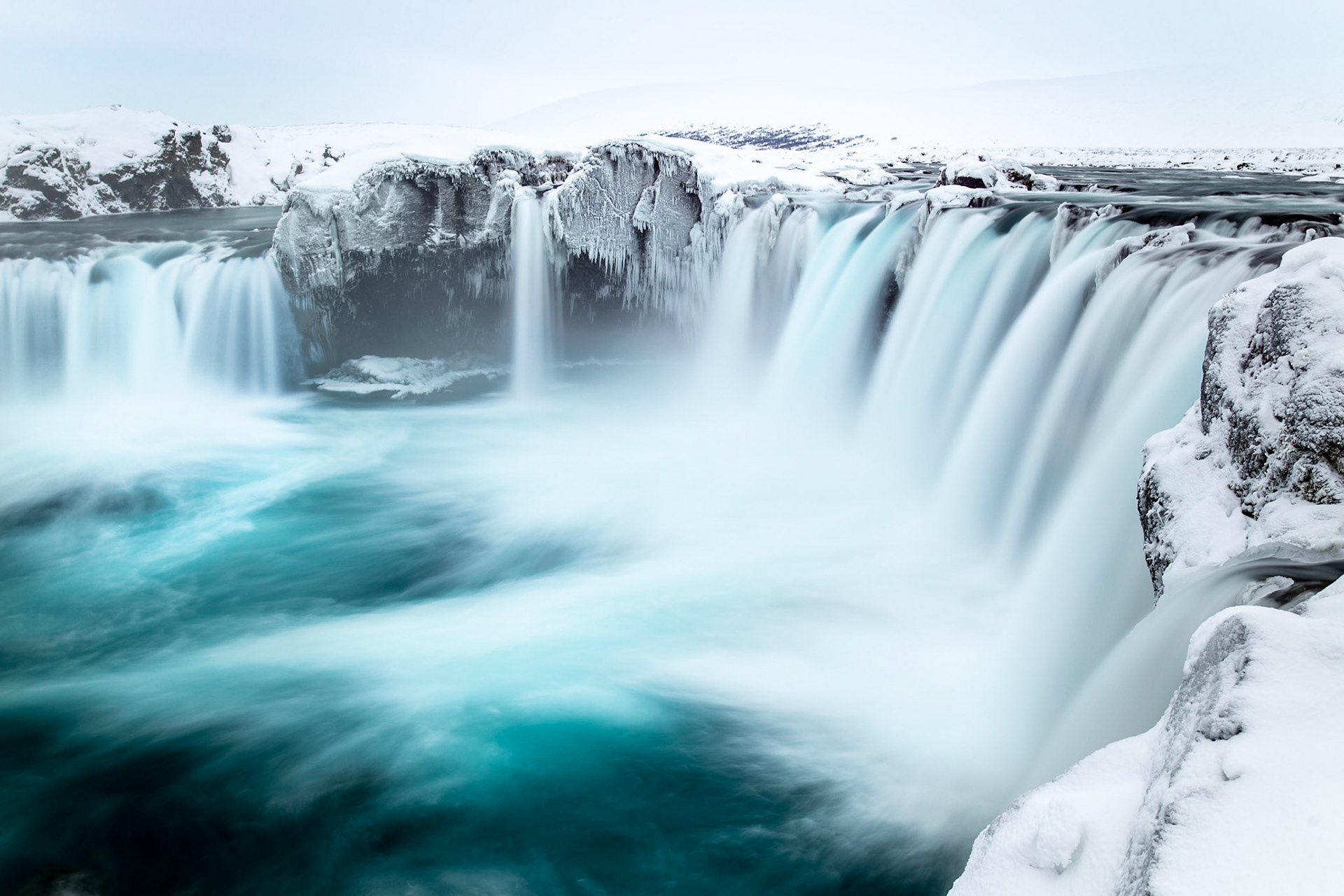 Glacial blue water flows smoothly in many streams over Godafoss creating ribbons of turquoise amidst the the ice and snow of winter.