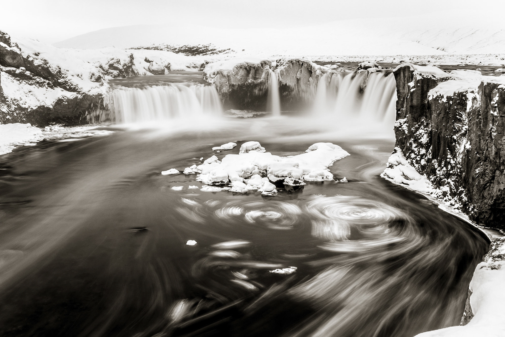 Water plunges smoothly in many streams over Godafoss creating ribbons of white amidst the the ice and snow and dark water of winter.