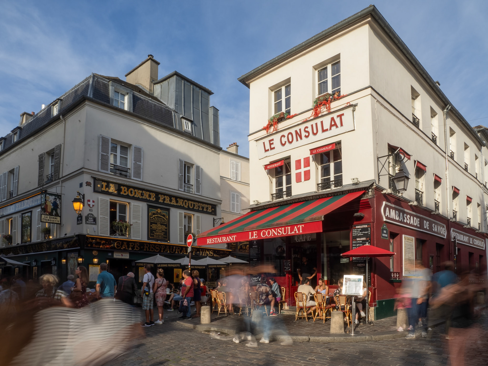The blurred moement of busy pedestrians in front of Le Consulat cafè while other sit enjoying the evening.