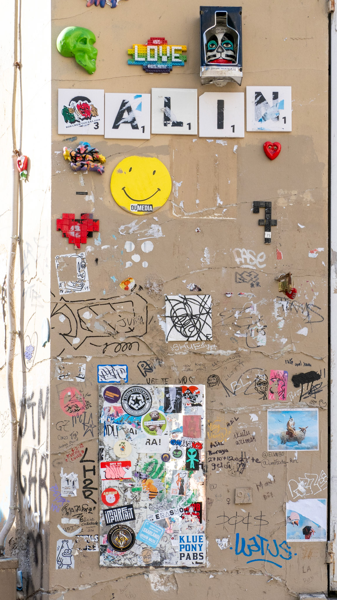 A beige wall is filled with the random scribblings, drawings, posters and words creating unique and detailed street art in Montmartre, Paris