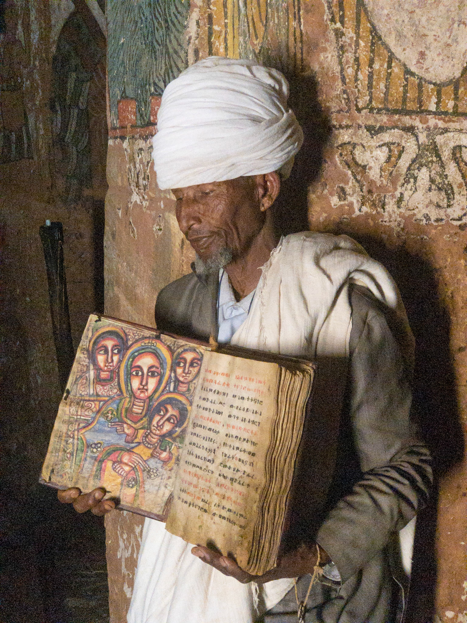 A priest holds an open bible with illumination in Abuna Yemata Guh monlithic rock-hewn church, Tigray, Ethiopia