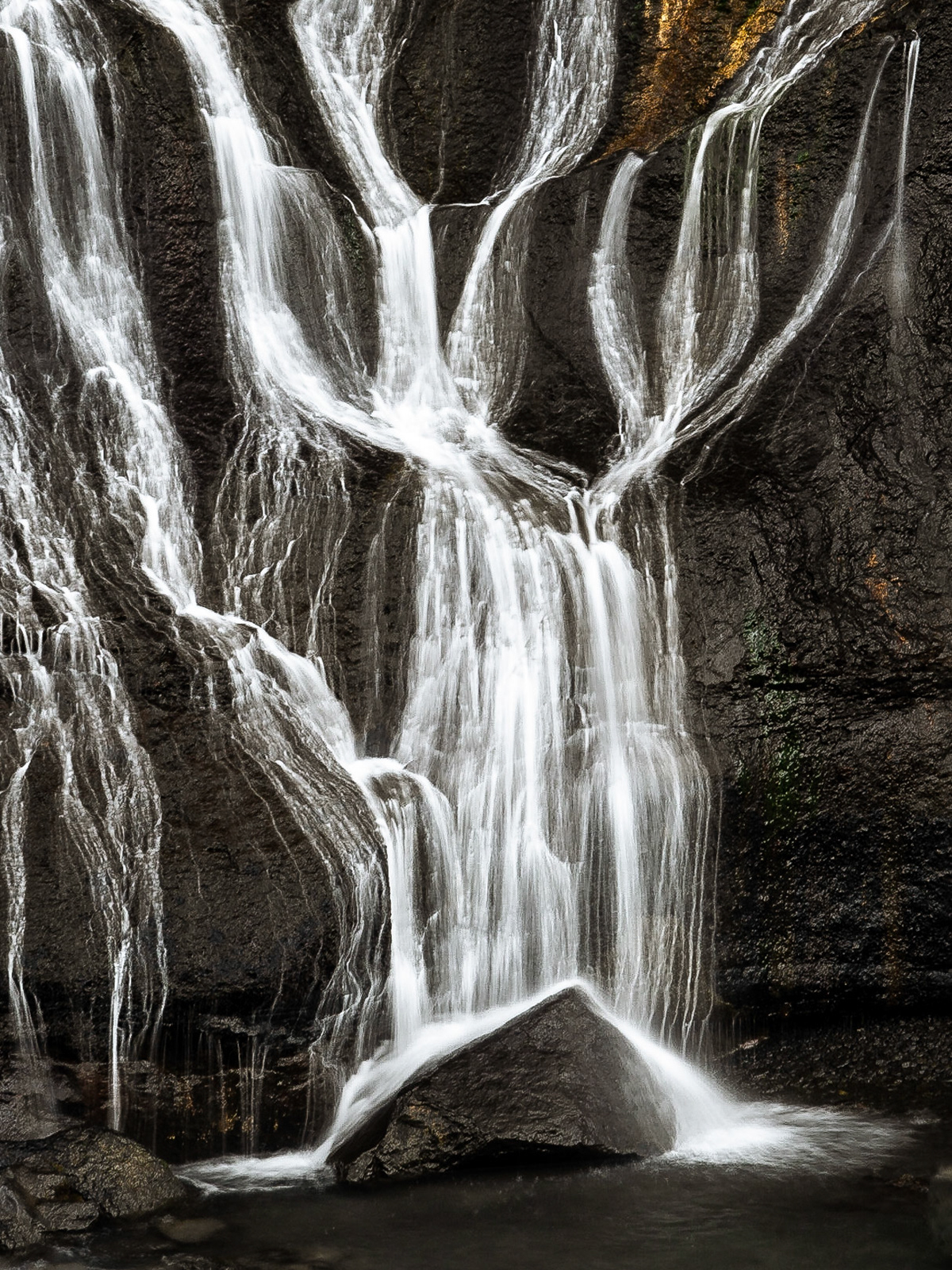 Ribbons of bright white water flow playfully over and in stark contrast to the dark, black lava at the Hraunfoss waterfall.