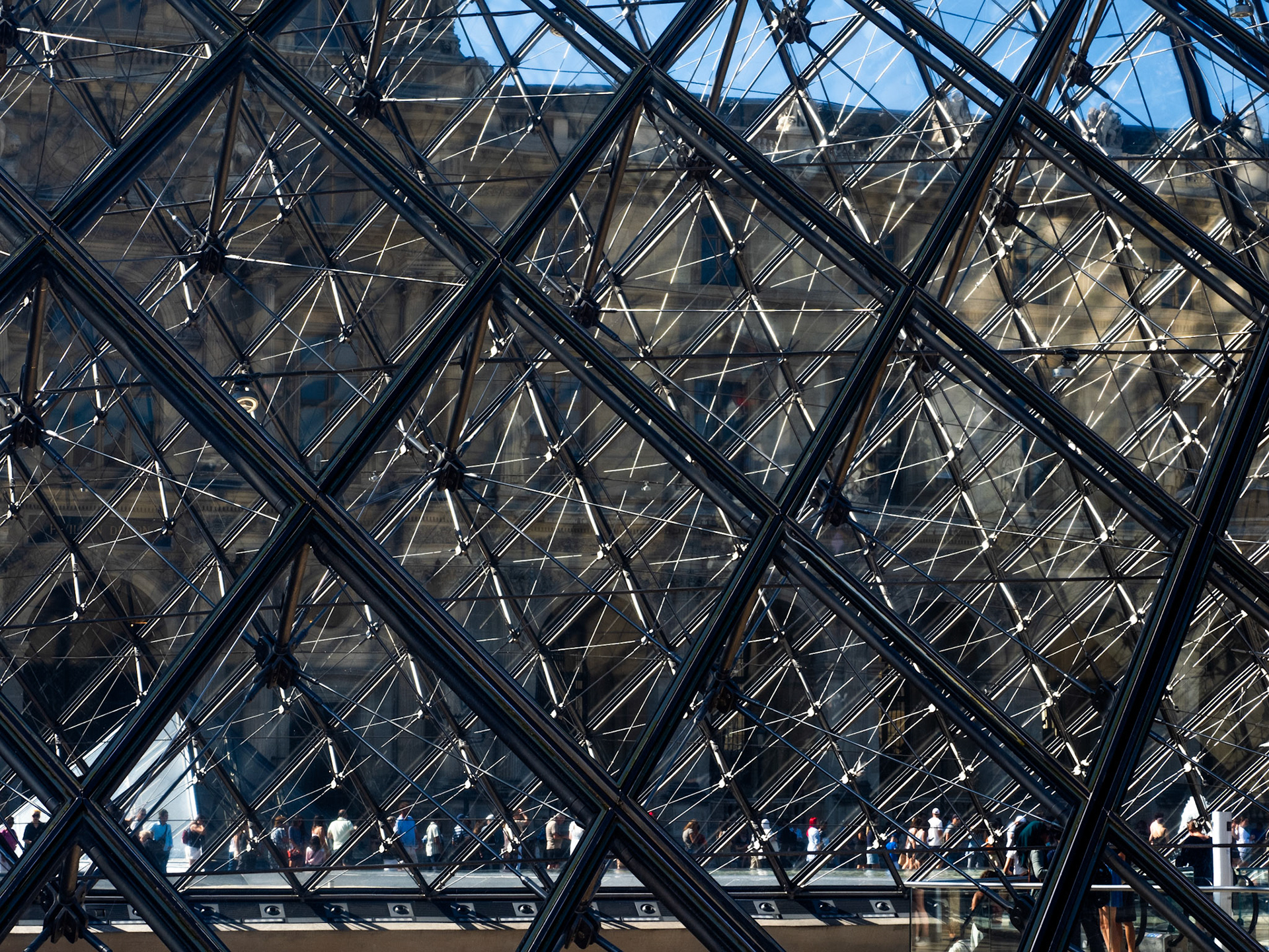 Amidst the jumble of diamonds and triangles created by the Louvre Pyramid, near the bottom of the image, a line of people queue for tickets