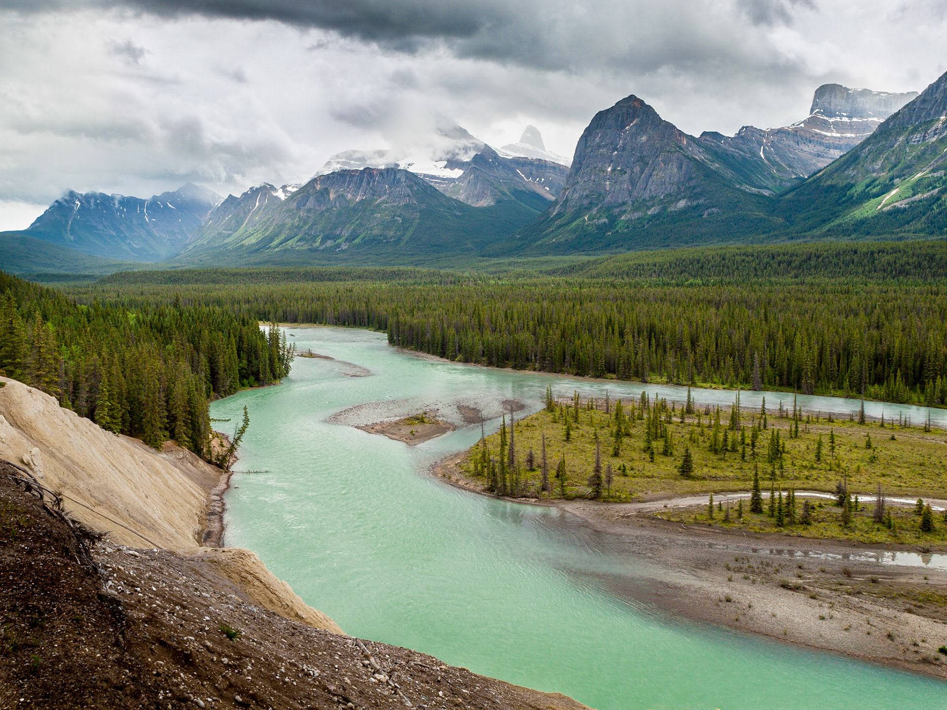 The glacier-fed, turquoise waters of the Athabasca River flowing northwards through Jasper National Park with the backdrop of the dramatic Rocky Mountains and coniferous-forest floodplain