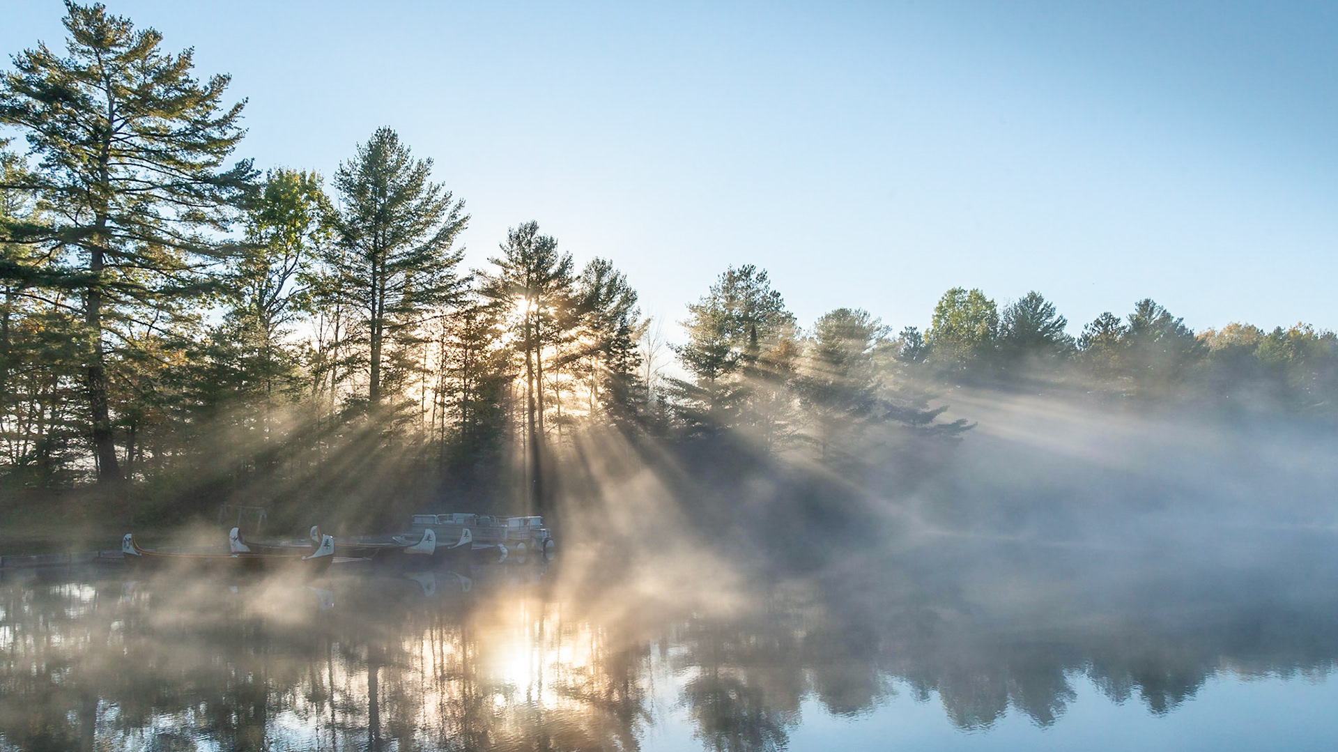 Sunlight streams through the white pines of the Canadian Shield falling on canoes at Bark Lake Leadership Centre, Irondale, Ontario