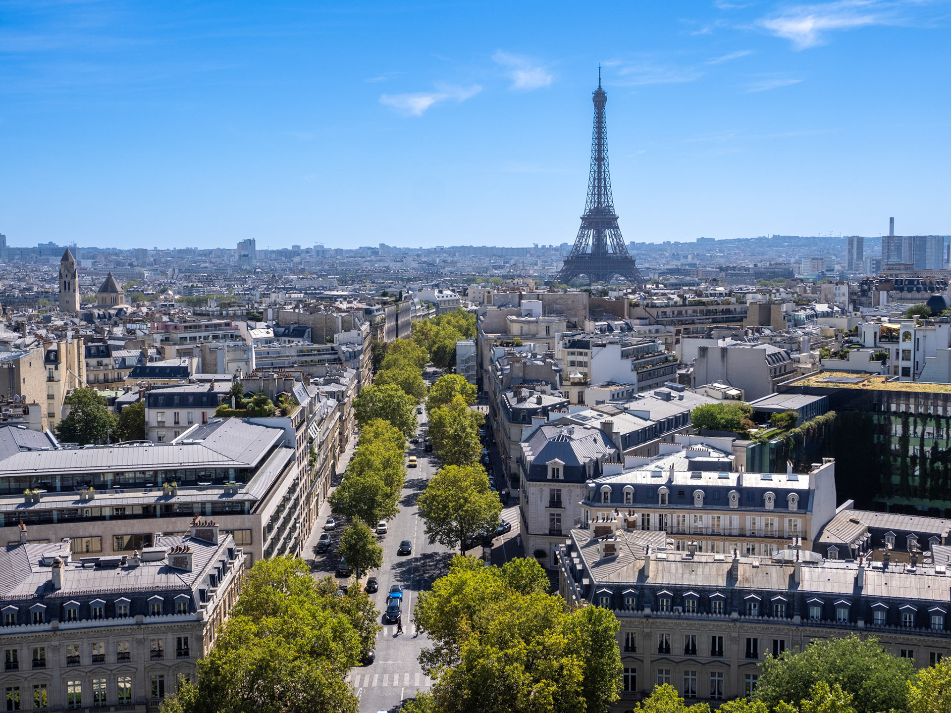 On a clear sky, summer day, the landmark Eiffel Tower stands proudly oave the currounding streets and apartments in Paris, France.
