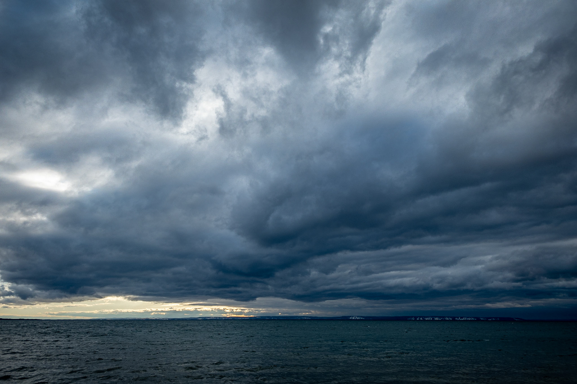 Dramatic, cold, wintery cloudy sky above a lake with yellow sunlight on the horizon