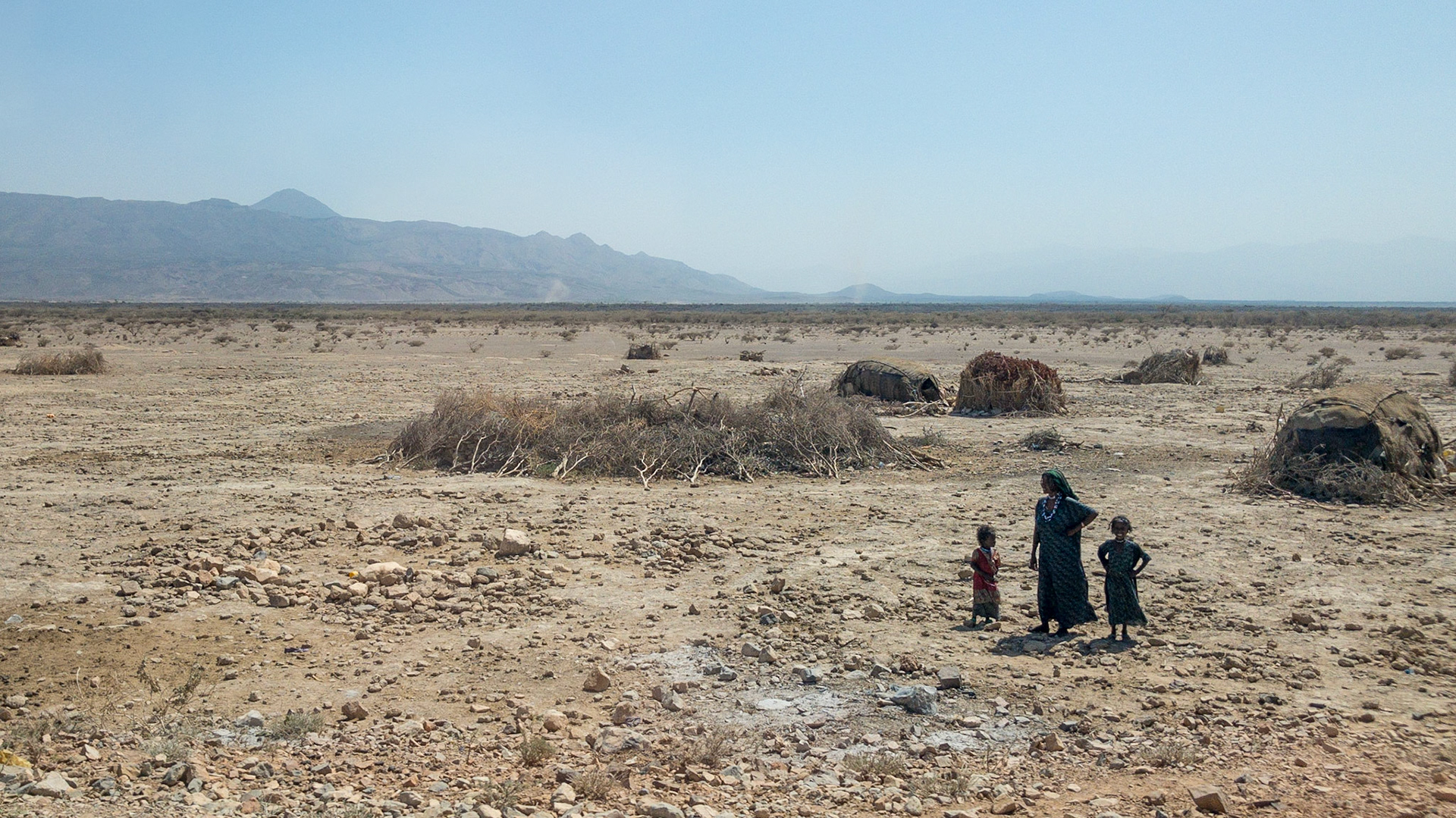 A woman and two young children stand in front of a scrub huts and a small corral in the Danakil Desert, in Ethiopia's Danakil Depression, the hottest, driest, most inhospitable place o Earth.