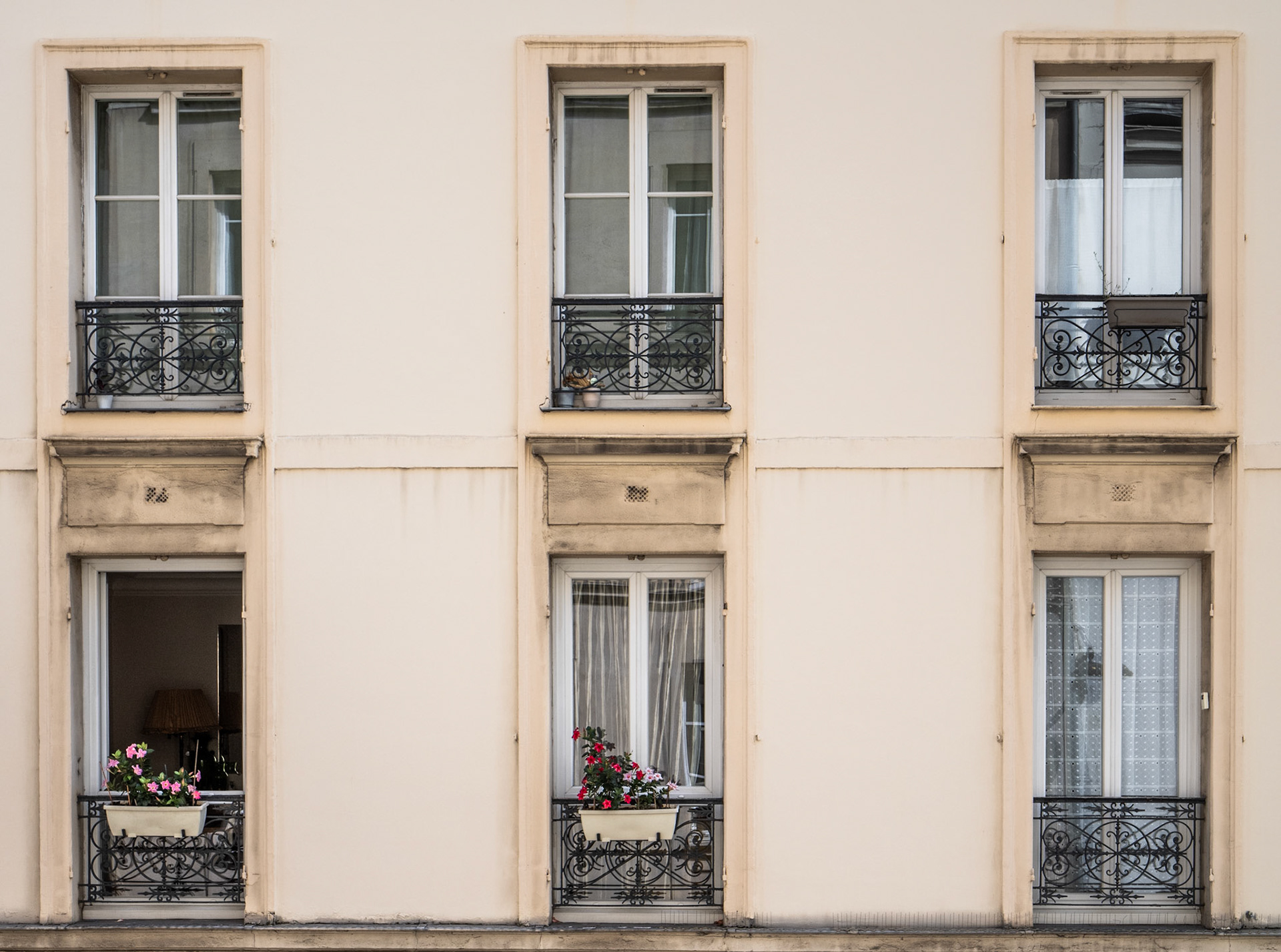Two flower boxes adorn a set of six rectangular windows spread over two floors of a Paris apartment building.