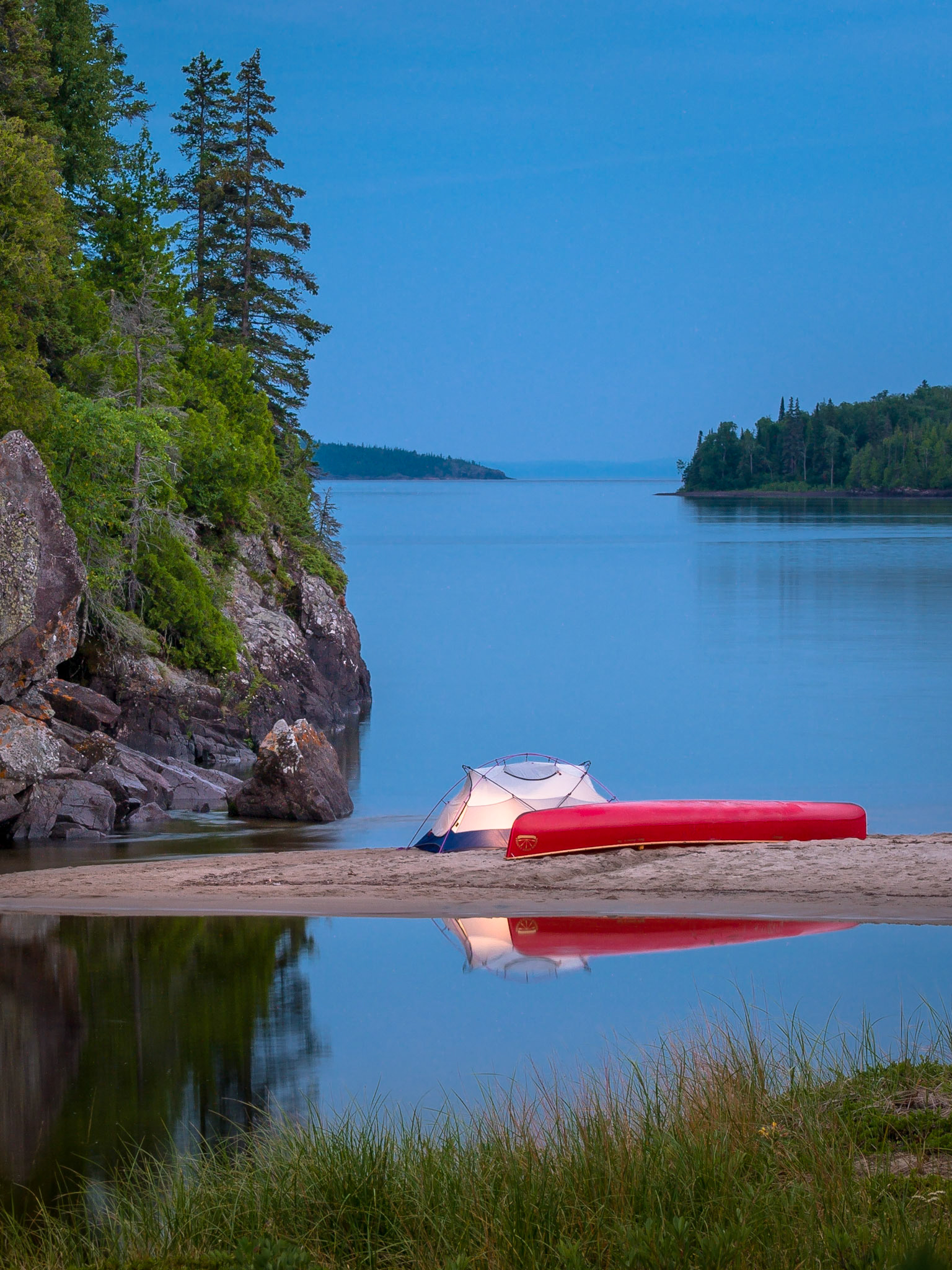 Candle-lit tent and canoe in summer evening light at dusk along the sandy shoreline of Warp Bay at the mouth of the Gargantua River, Lake Superior in Lake Superior Provincial Park, Ontario, Canada
