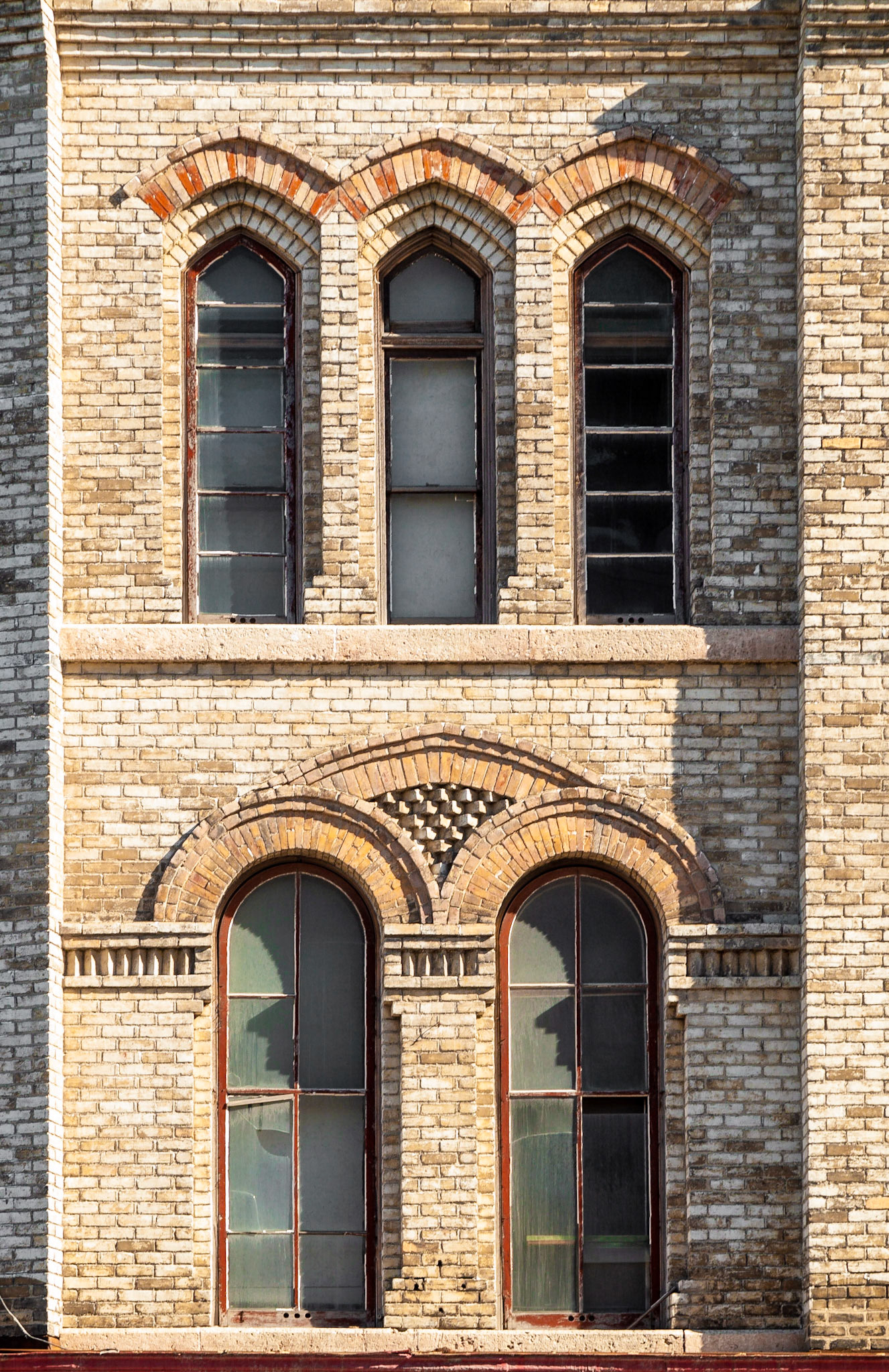 Mottled yellow brick building with ornate brickwork above round-topped  windows in the Exchange District, Winnipeg, Manitoba, Canada