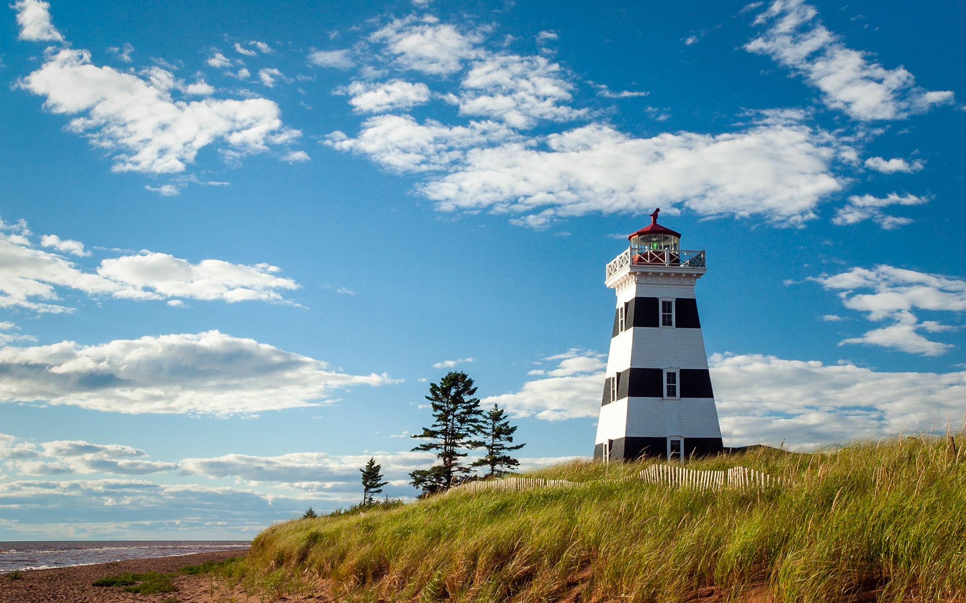 Black and white lighthouse on grass-covered dunes with pine trees on the southwest coast of Prince Edward island, Canada