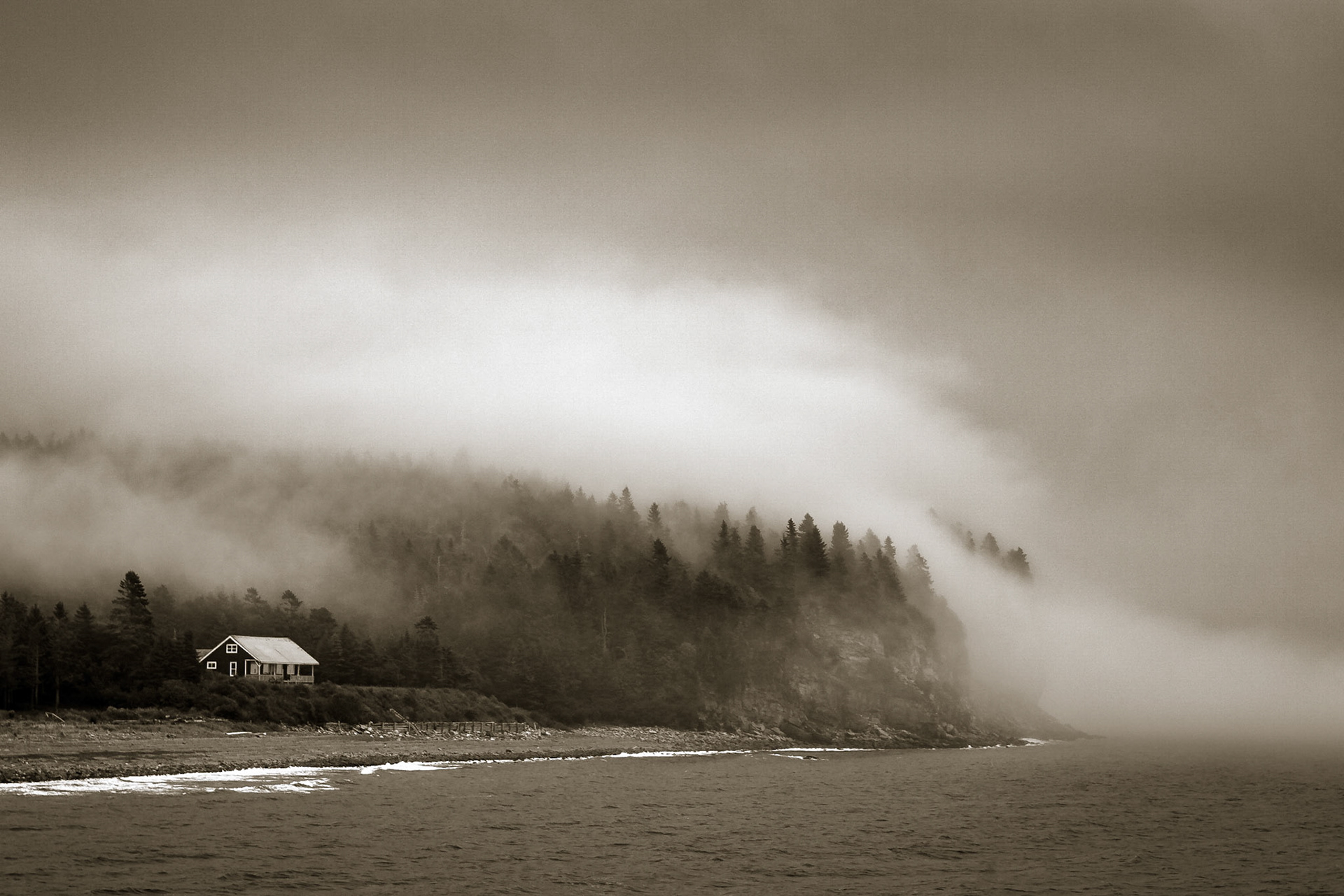 A lone house sits amongst the forests of the Bay of Fundy coast, New Brunwick, Canada, as fog rolls in from the sea