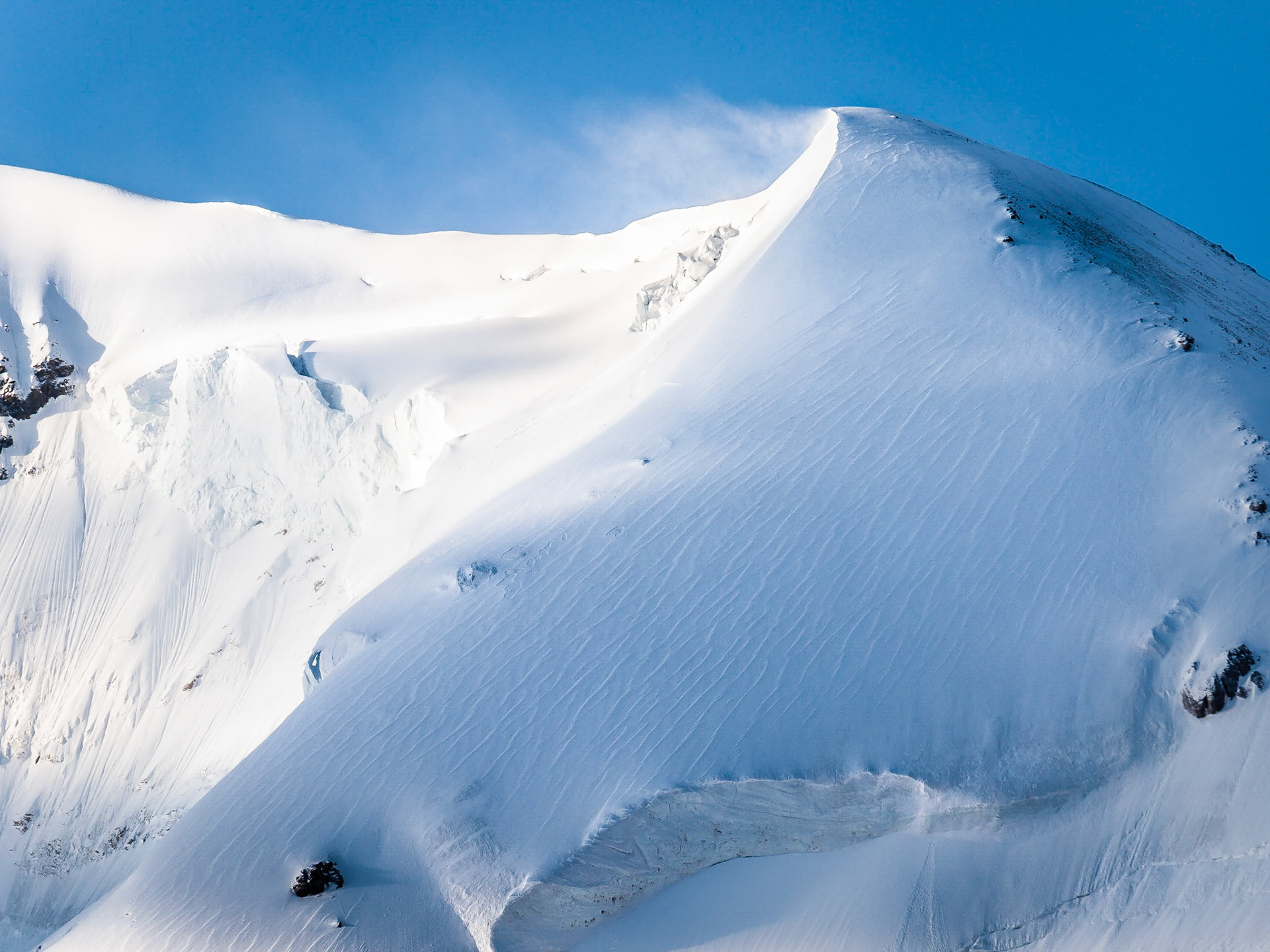 A plume of snow is blown off the trianular, snow-covered peak of Mount Saskatchewan, above the Columbia Icefields in Jasper National Park, Alberta, Canada
