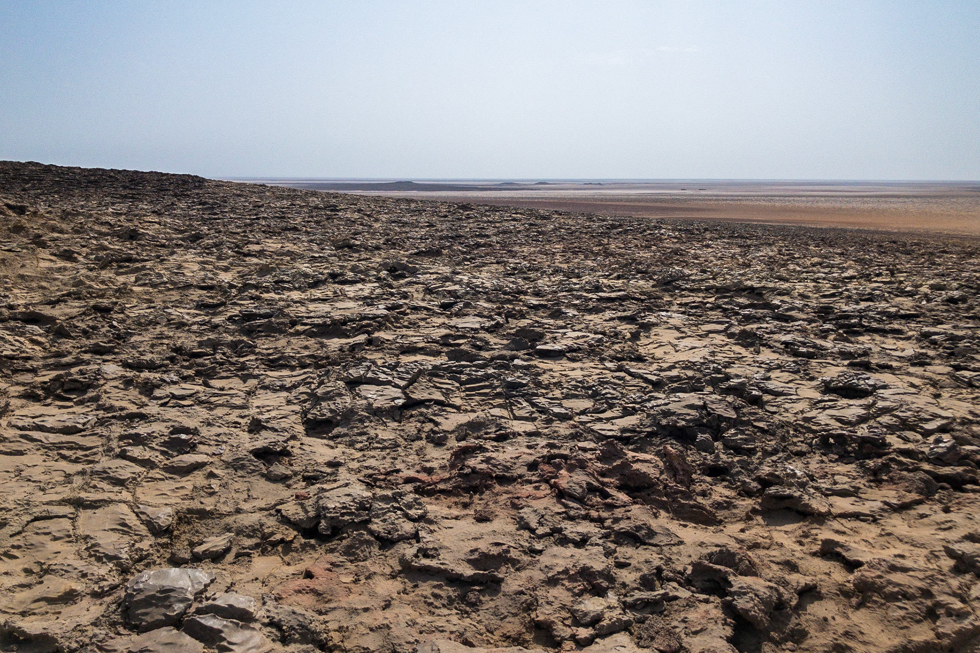 Grey, eroded lava spreads out in the foreground with the great Danakil Depression, Ethiopia, stretching to a desolate horizon, the hottest, driest, most inhospitable place on Earth.