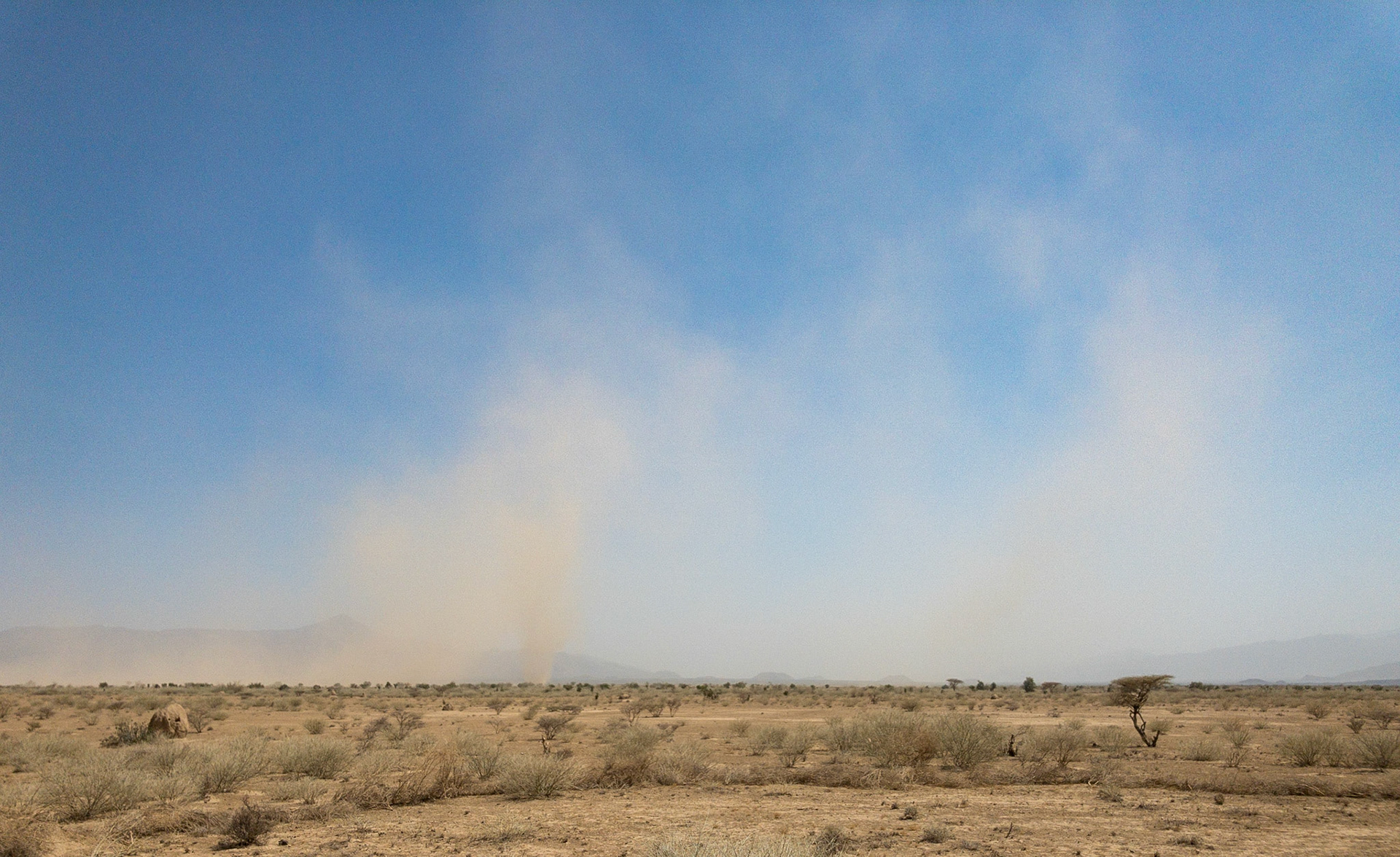 Plumes of dust rise high intoa. clear blue sky above the scrubby Danakil Desert in Ethiopia's Danakil Depression, the hottest, driest, most inhospitable place on Earth.