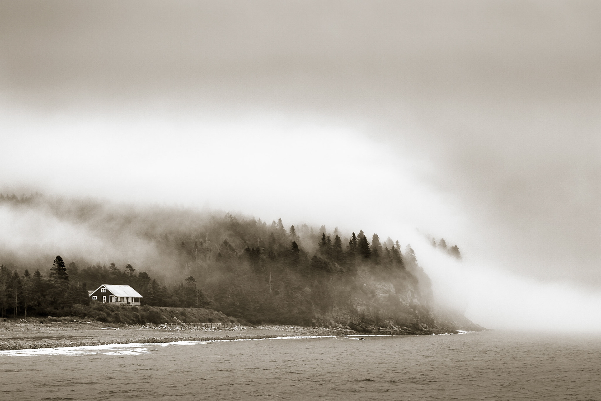 A lone house sits amongst the forests of the Bay of Fundy coast, New Brunwick, Canada, as fog rolls in from the sea
