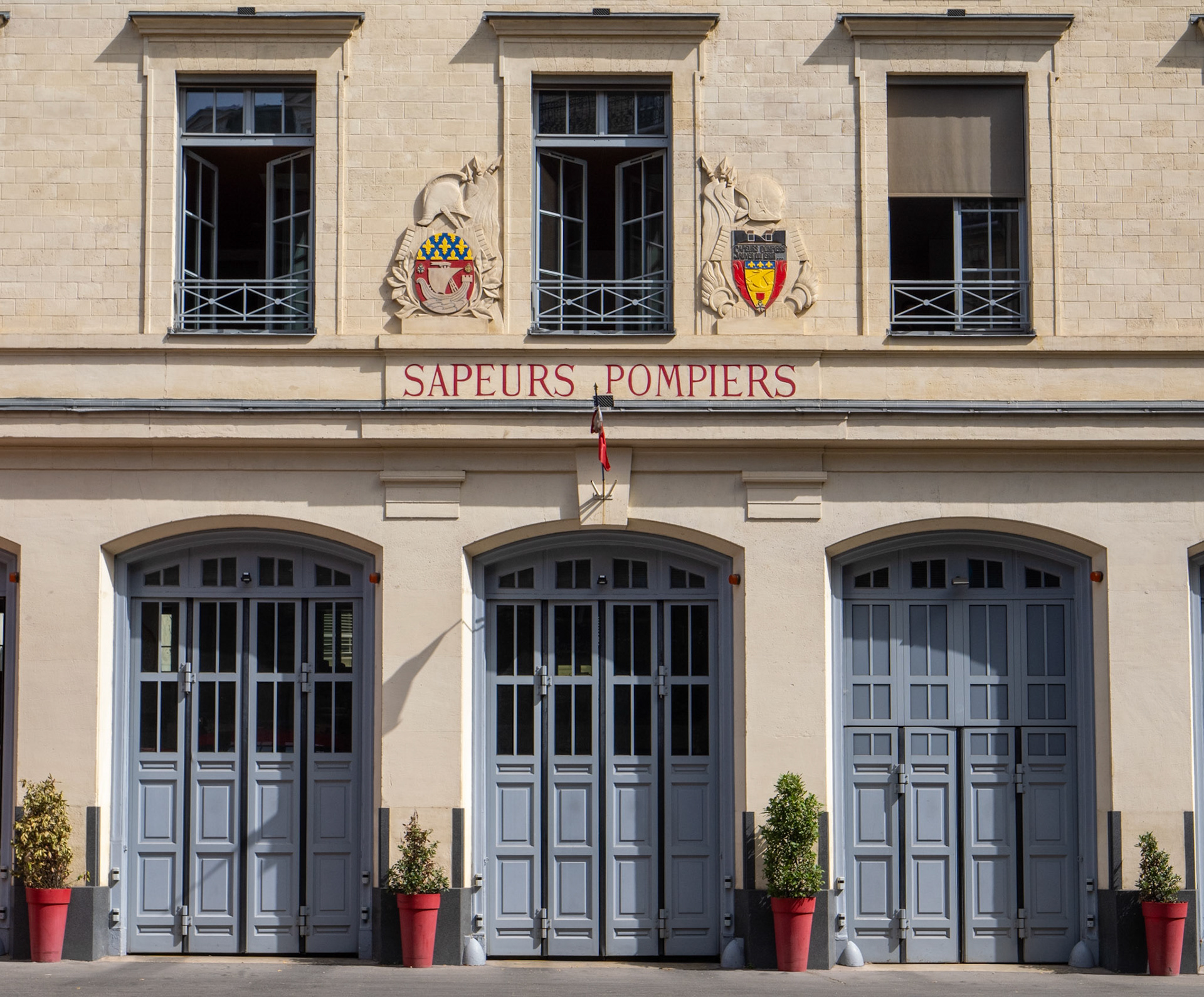 The ordered, rectangualr desing of the front of a Paris fire station with three upper windows and three garage doors.