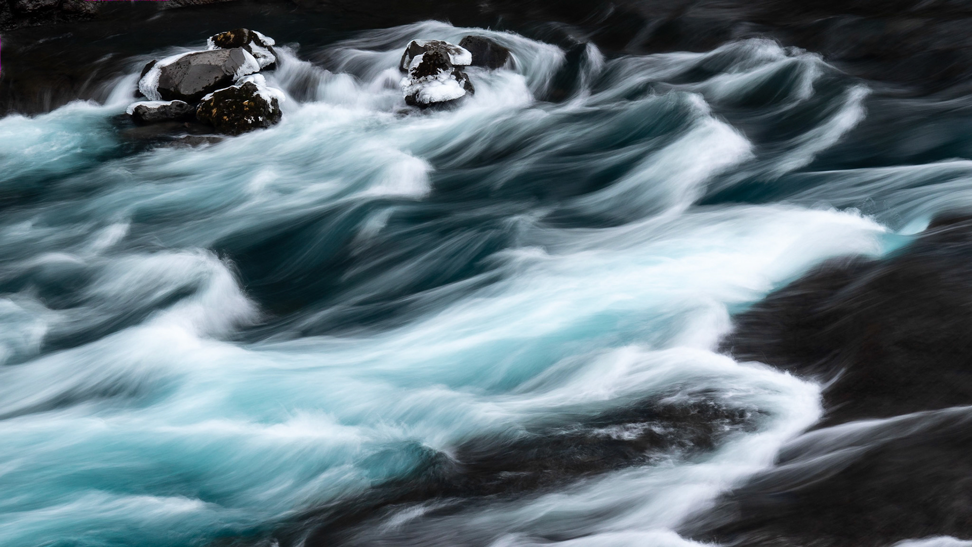 The glacial blue Hvita River flows gracefully over the dark lava rock of the riverbed creating ribbons of turquoise and white against the dark river