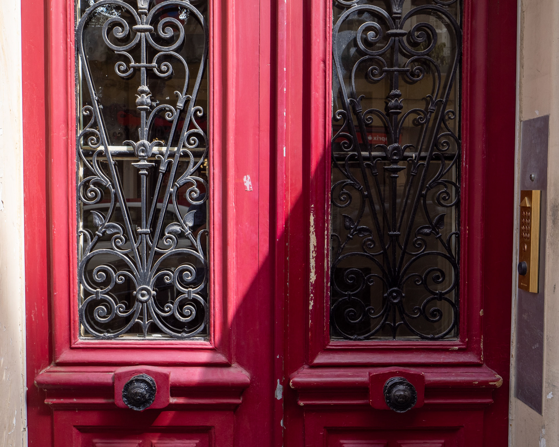 A close-up of the handles and glass of twin red doors on a Paris street with angular lighting.