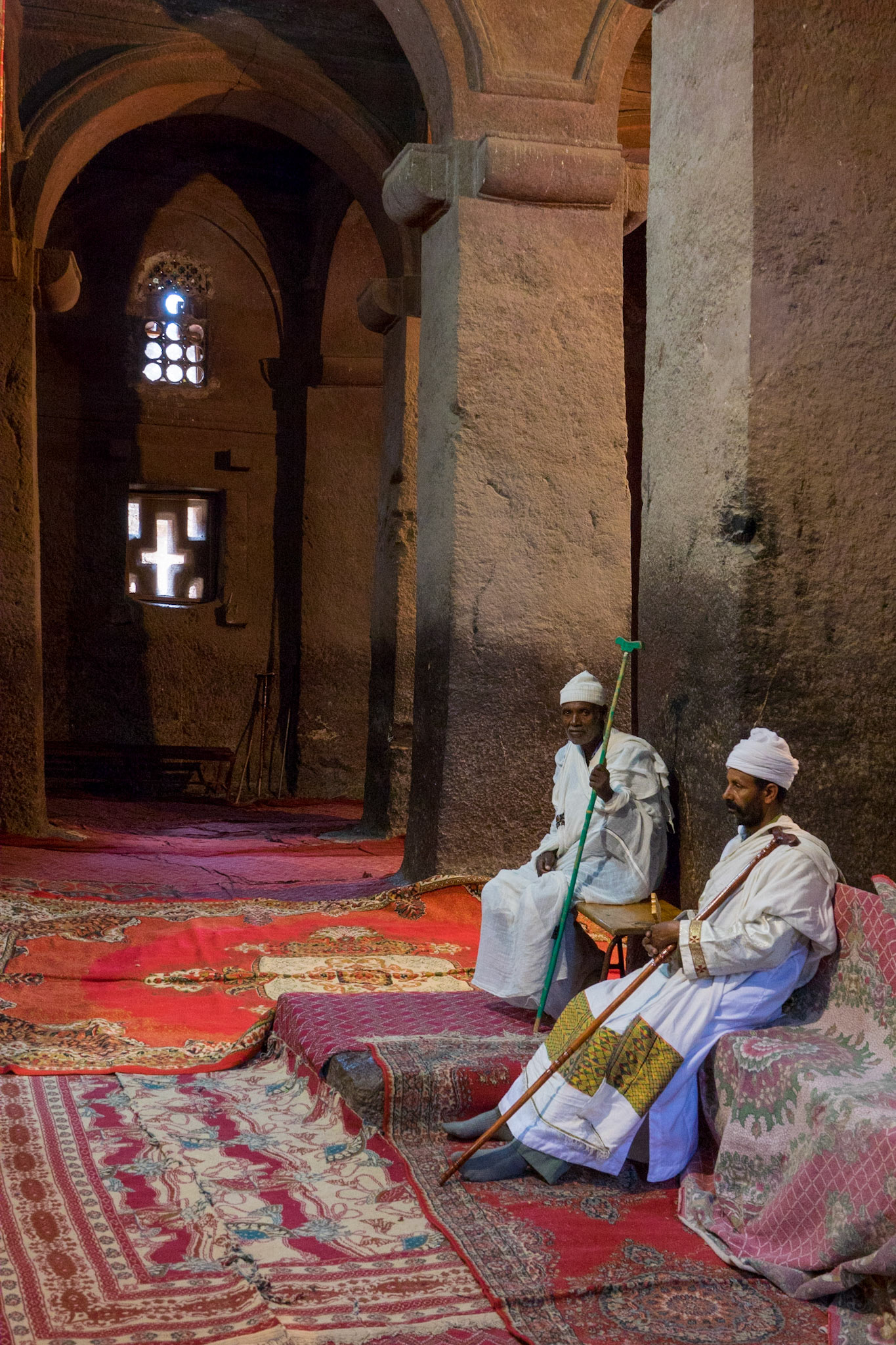 A priest and a monk sit inside amongst the rock-hewn pillars of Biete Medhane Alem, Lilibela, Ethiopia