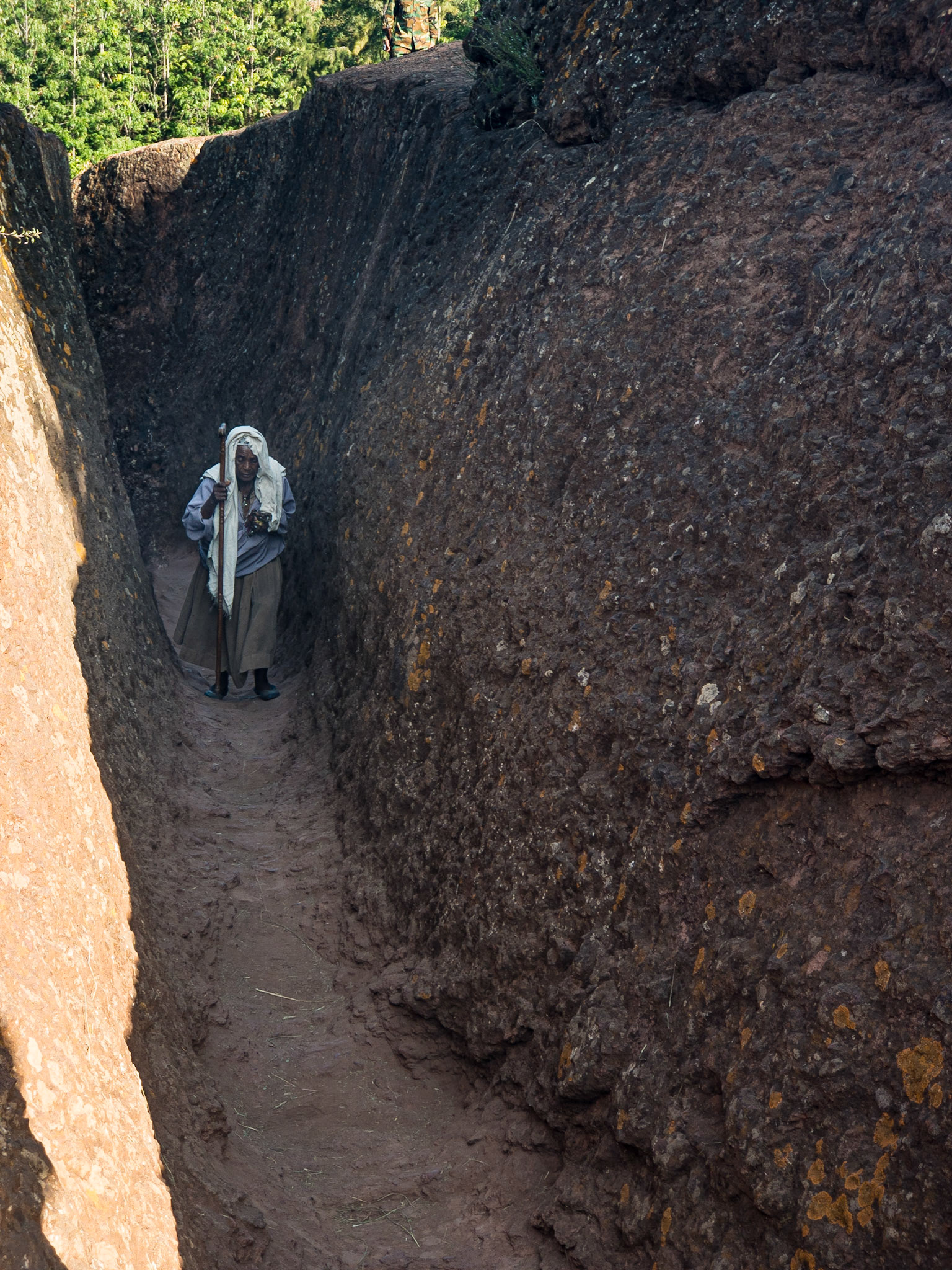 A lone old waoman navigates the rock-hewn channel-like walkway of Biete St. Giyorges, Lalibela, Ethiopia