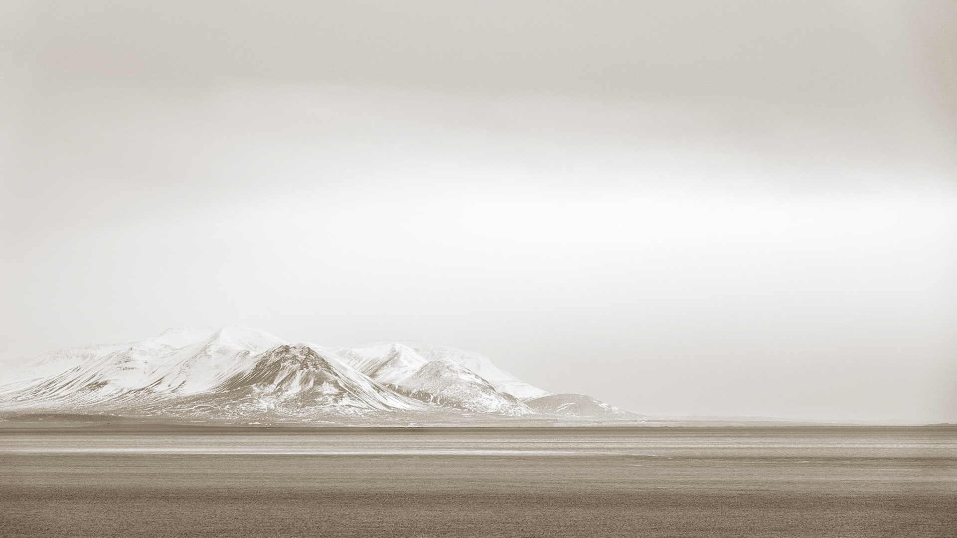 The snow-covered mountains of the Vatnsnes peninsula and shrouded in misty fog and cloud as they appear in the distance across the bay.