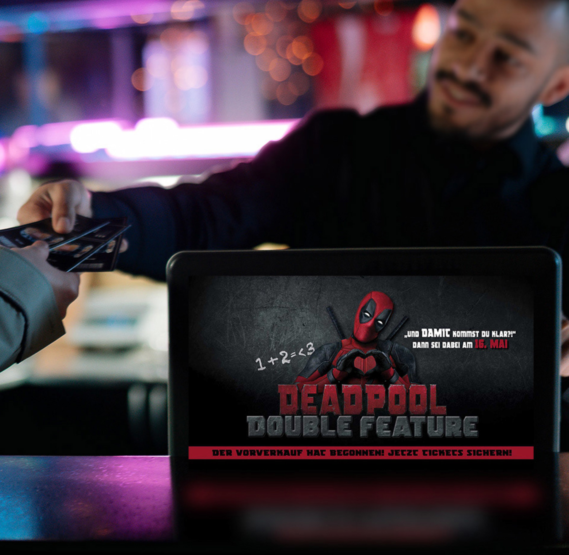 Vorverkaufsankündigung für Deadpool Doublefeature, Verkäufer händigt Karten an Kunden aus.