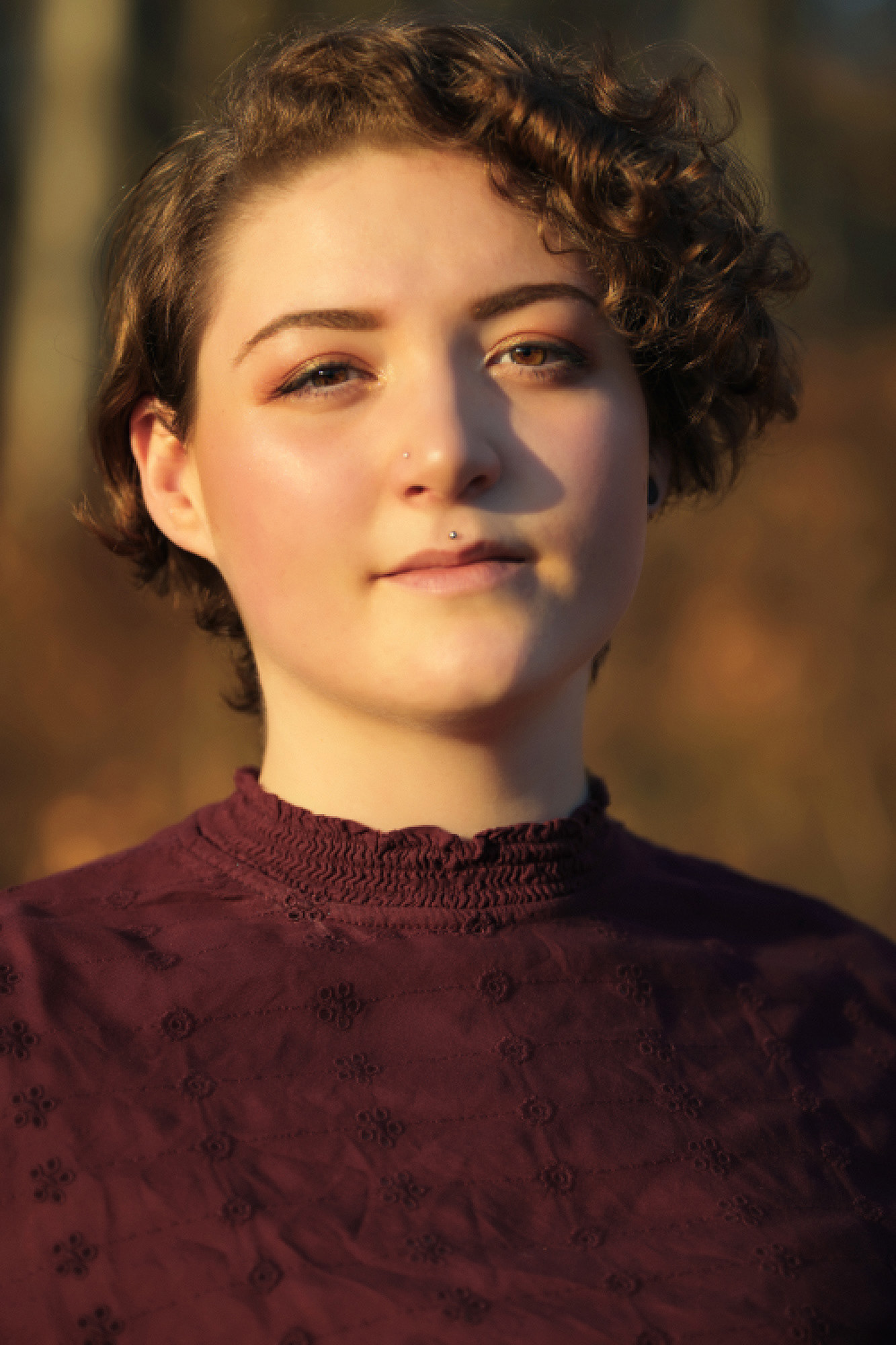 Portrait von Rebeka Schiessl, im Wald umgeben von warmen Herbsttönen und dezentem goldenem Licht des Sonnenuntergangs.