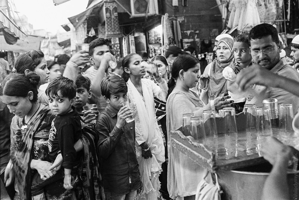 In the middle of a hot day, a rose water merchant attracts numerous customers seeking the popular Indian refreshing beverage.