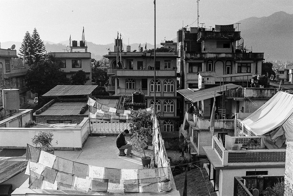 A man takes a moment to read on the rooftop of a Kathmandu house, enjoying a peaceful retreat from the hustle and bustle of the city below.