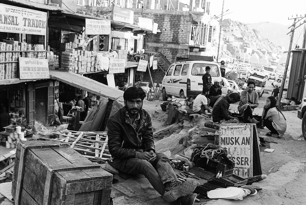 Amidst the lively trading street of Leh city, a shoemaker eagerly awaits the arrival of customers.