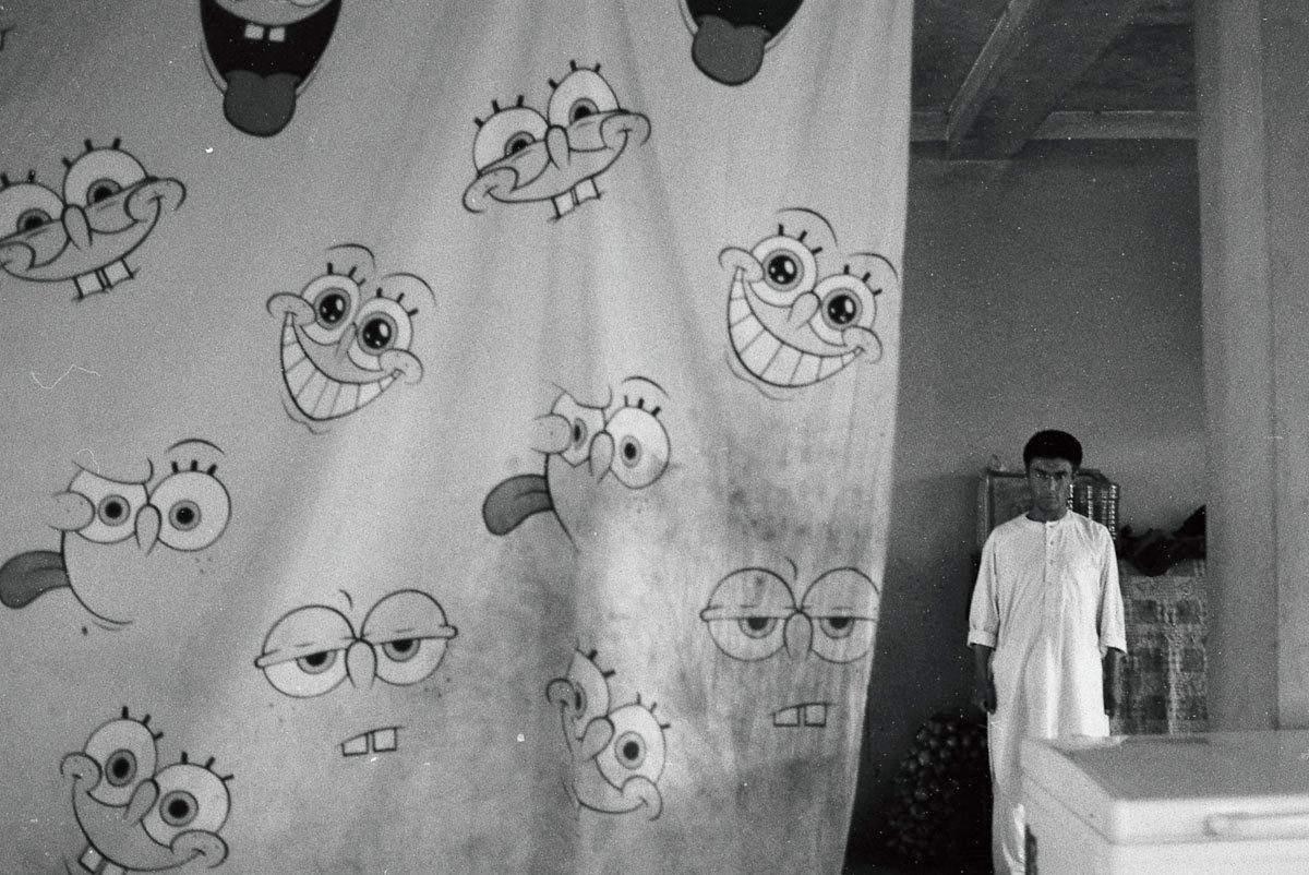 Waiter serves up a hot cup of chai in an Afghan roadside cafe, where a SpongeBob SquarePants curtain adds a whimsical touch to the rustic surroundings.
