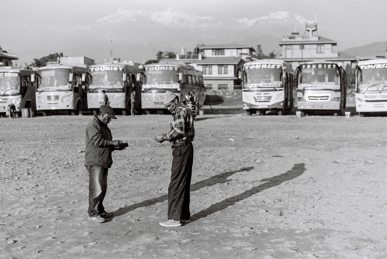 Bus drivers unwind with a game at the Pokhara tourist bus park, surrounded by the breathtaking Annapurna range in the distance.
