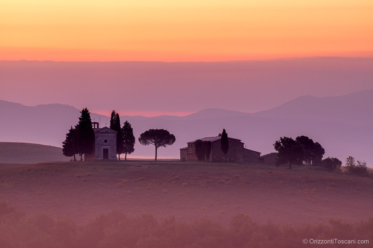 Cappella della Madonna di Vitaleta in Val d’Orcia, vicino a San Quirico d’Orcia, avvolta da foschia serale e toni rosa e viola, stampa paesaggistica toscana ideale per luxury resort, boutique hotel e interni esclusivi.