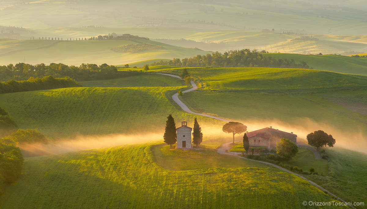 Veduta della Cappella della Madonna di Vitaleta in Val d’Orcia, vicino a San Quirico d’Orcia, immersa nella luce del mattino e nella nebbia soffusa, perfetta come stampa d’arte per luxury resort, boutique hotel e interni esclusivi.