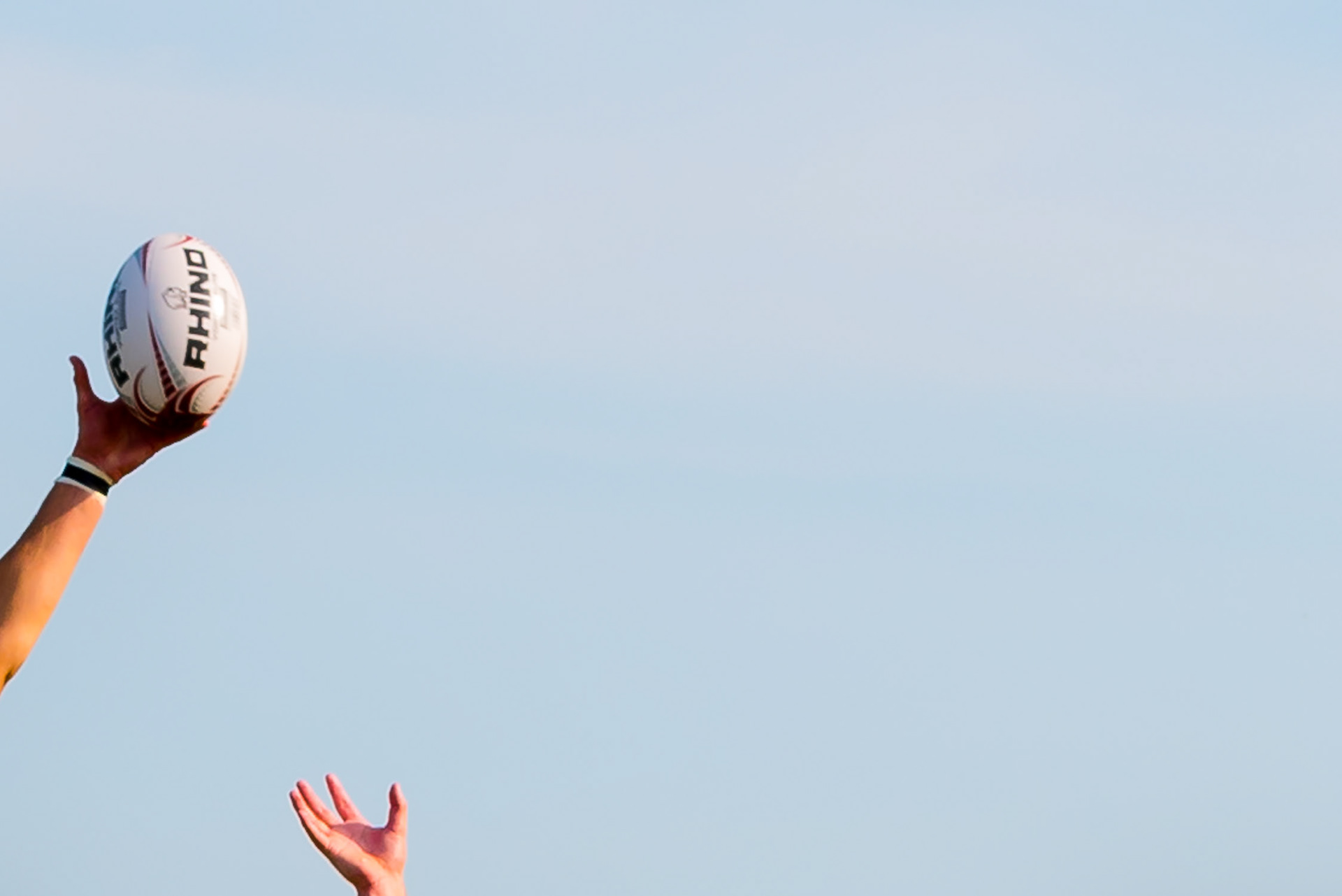 A cropped image with only two hands stretching / reaching for a rugby ball in flight