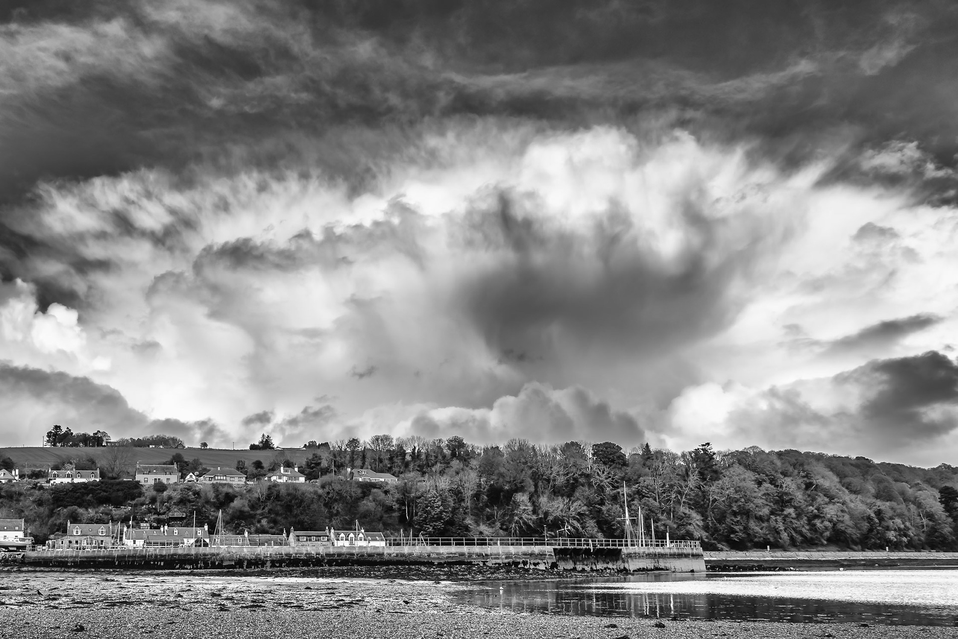 A black and white image of an enormous cloud gathering behind the small village and harbour of Avoch, Black Isle, Scottish Highlands
