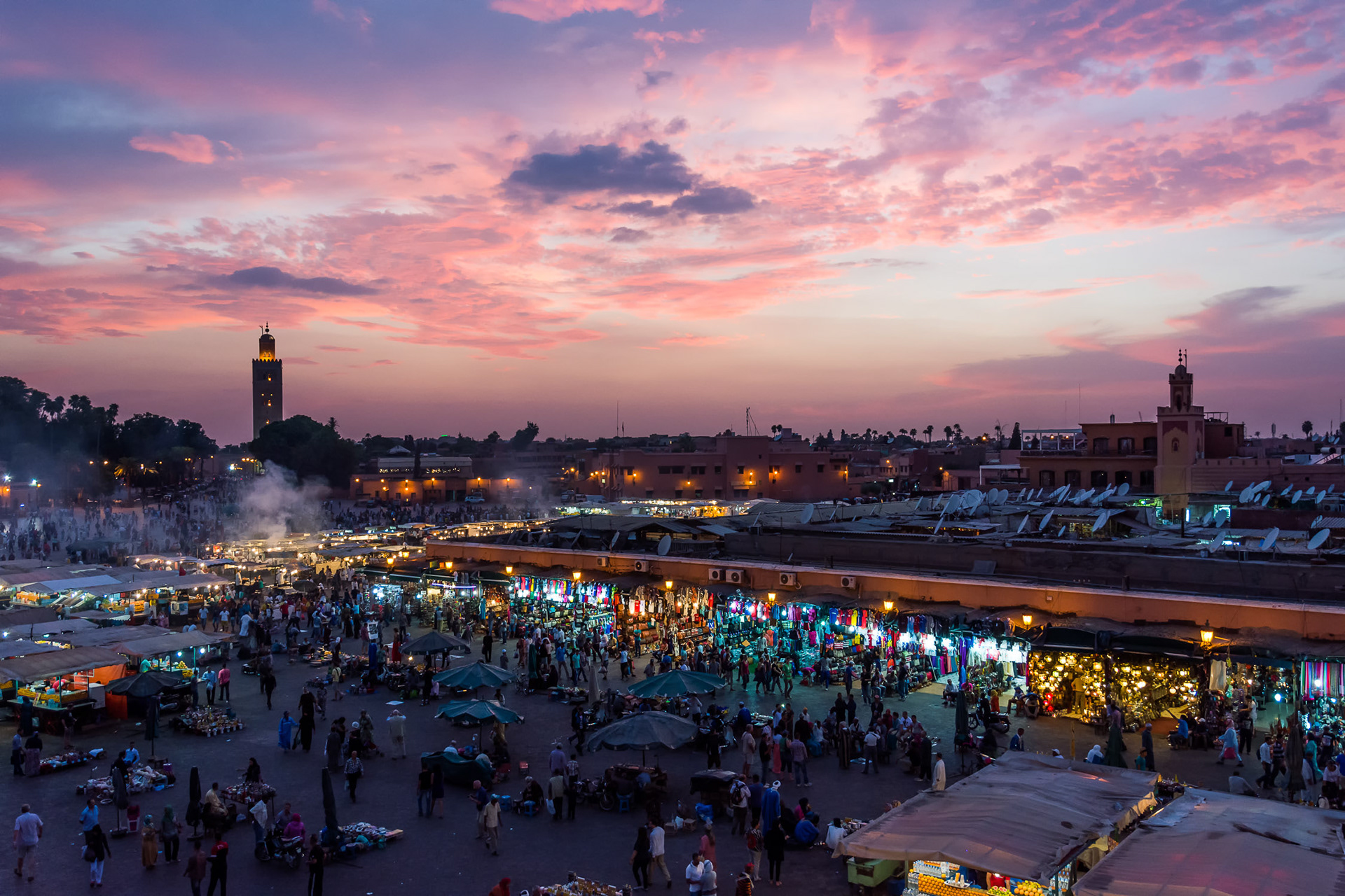 An elevated view of the Jemaa el Fnaa market square in Marrakesh at sunset. The pastel colours in the sky provide some gentle light as the food stalls and market stalls start to attract throngs of tourists