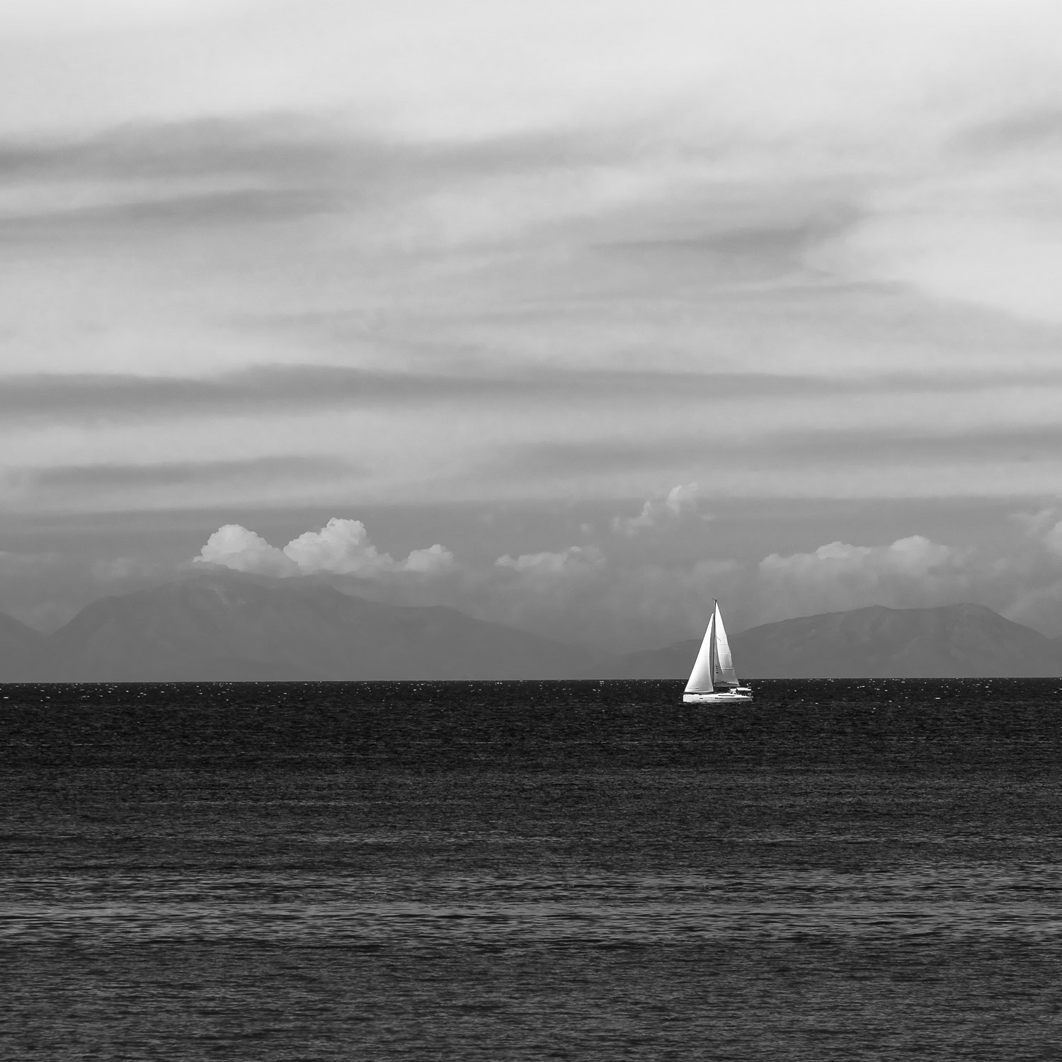 A black and white photo of a white sailboat on the azure blue waters of the Ionian Sea