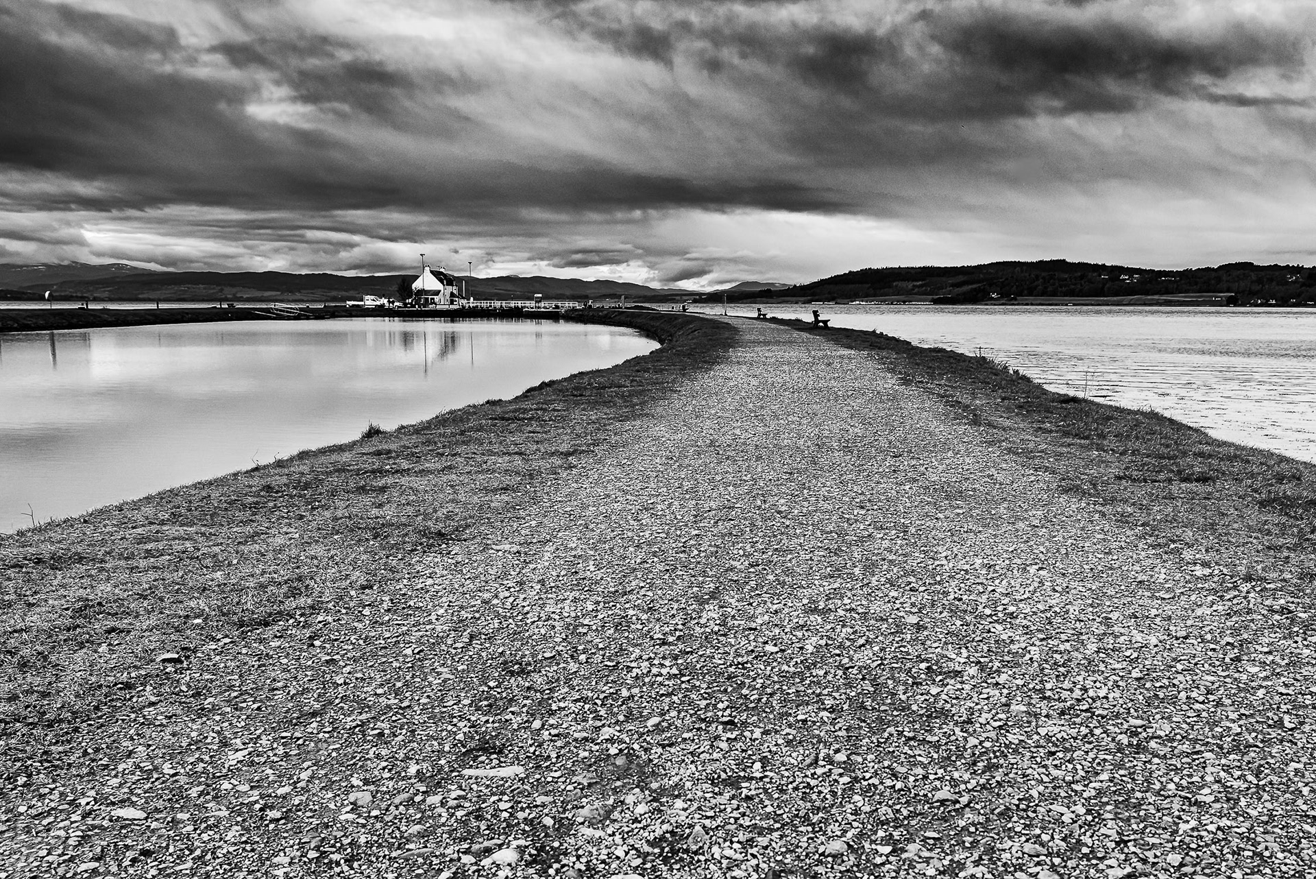 Under a stormy sky, the canal path alongside the Caledonian Canal on the left, and the Beauly Firth on the right, the path leading to the Clachnaharry Sea Locks at Inverness. Black and white image