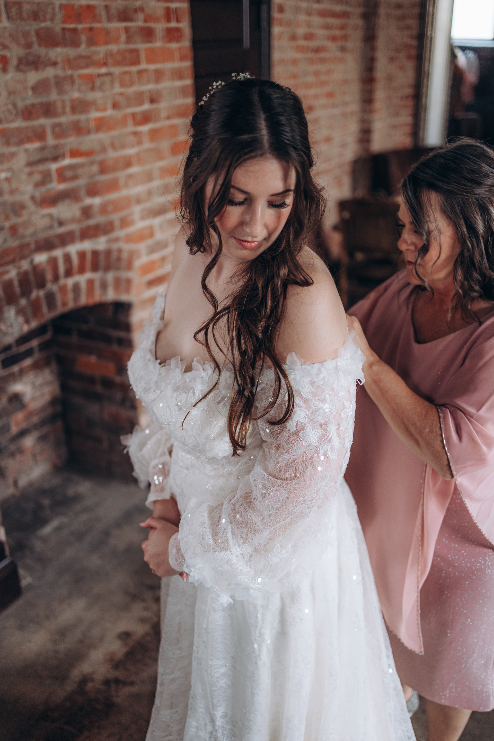 The mother of the bride assists her daughter in zipping up her beautiful wedding dress.