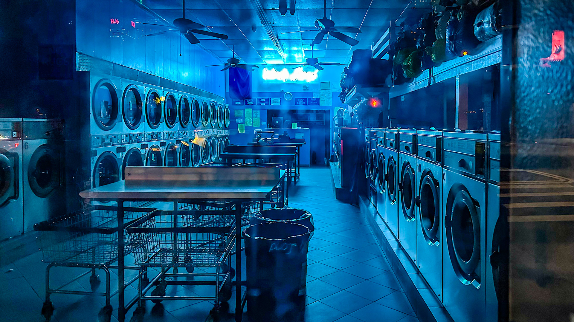 New York, NY, US - Sep 30, 2023: Empty laundromat lit by blue light at night with street reflection in window