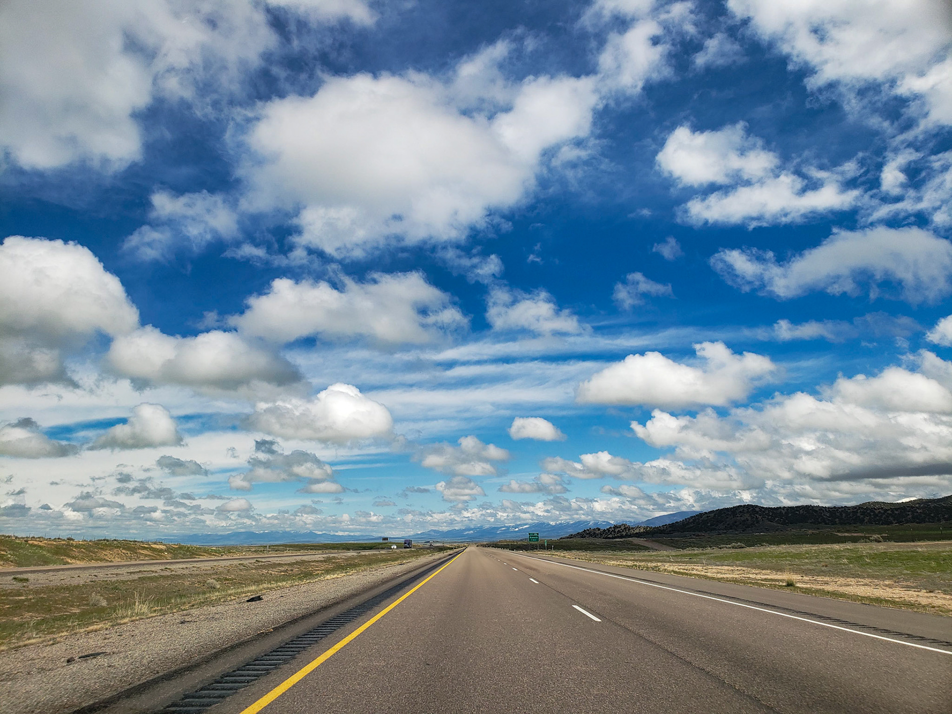 Kanosh, UT, US - Apr 6, 2019: Flat road with distant mountains and puffy white clouds in blue sky