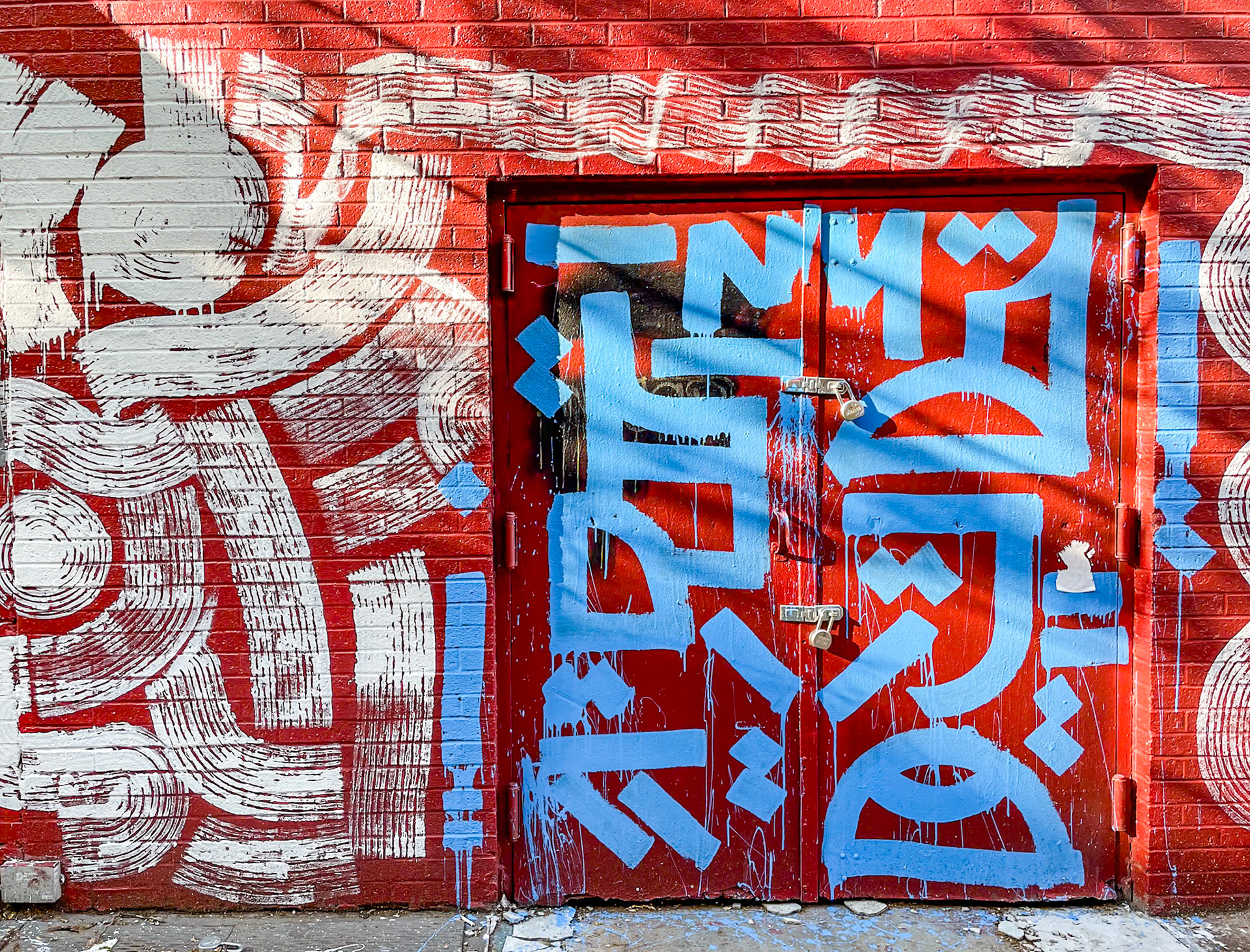 New York, NY - Jun 4, 2022: Abstract street art, blue paint on red door, white paint on red brick