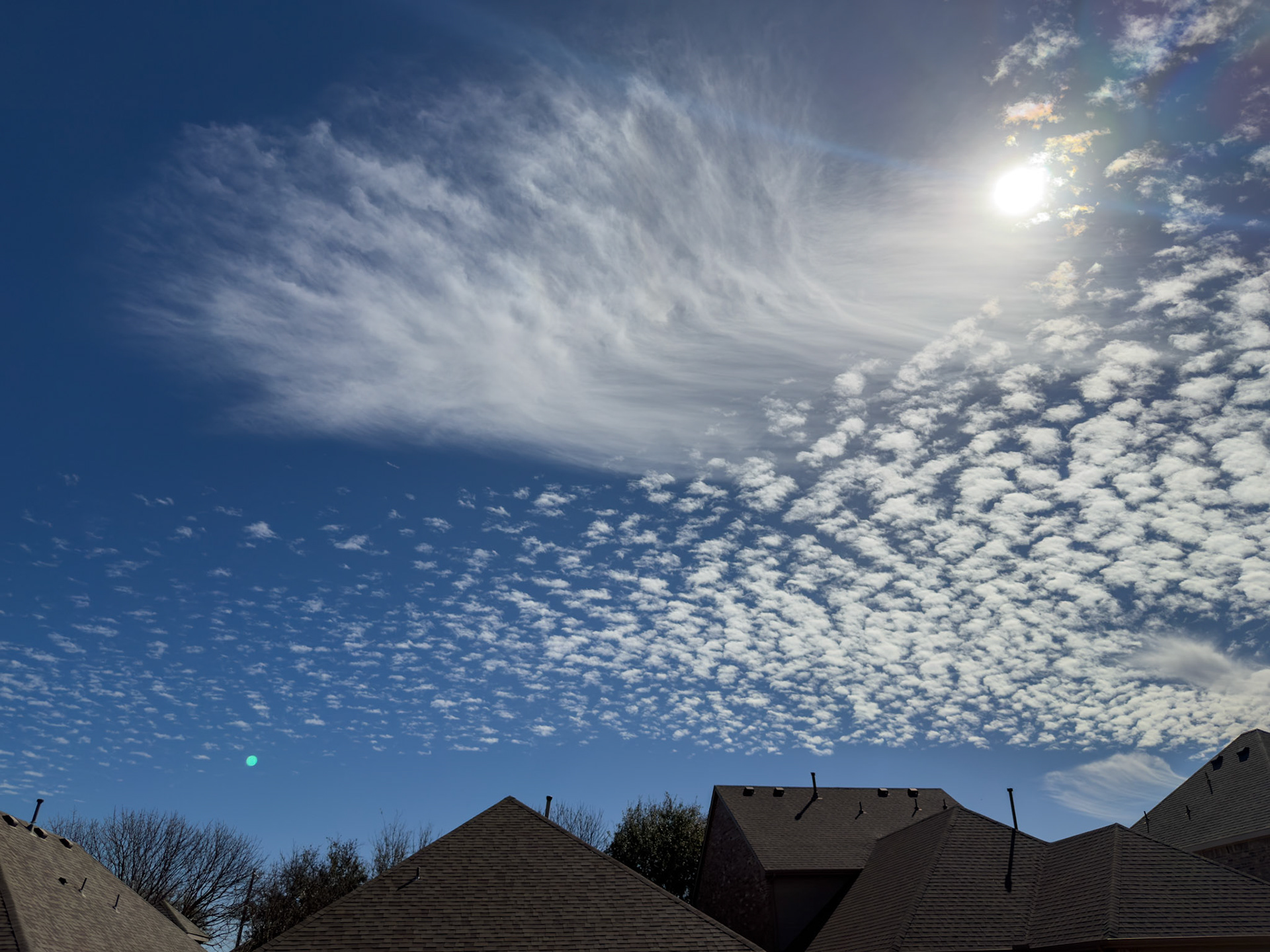 McKinney, TX, US - Feb 19, 2026: Sun shining through cirrus and cumulus clouds above suburban rooftops