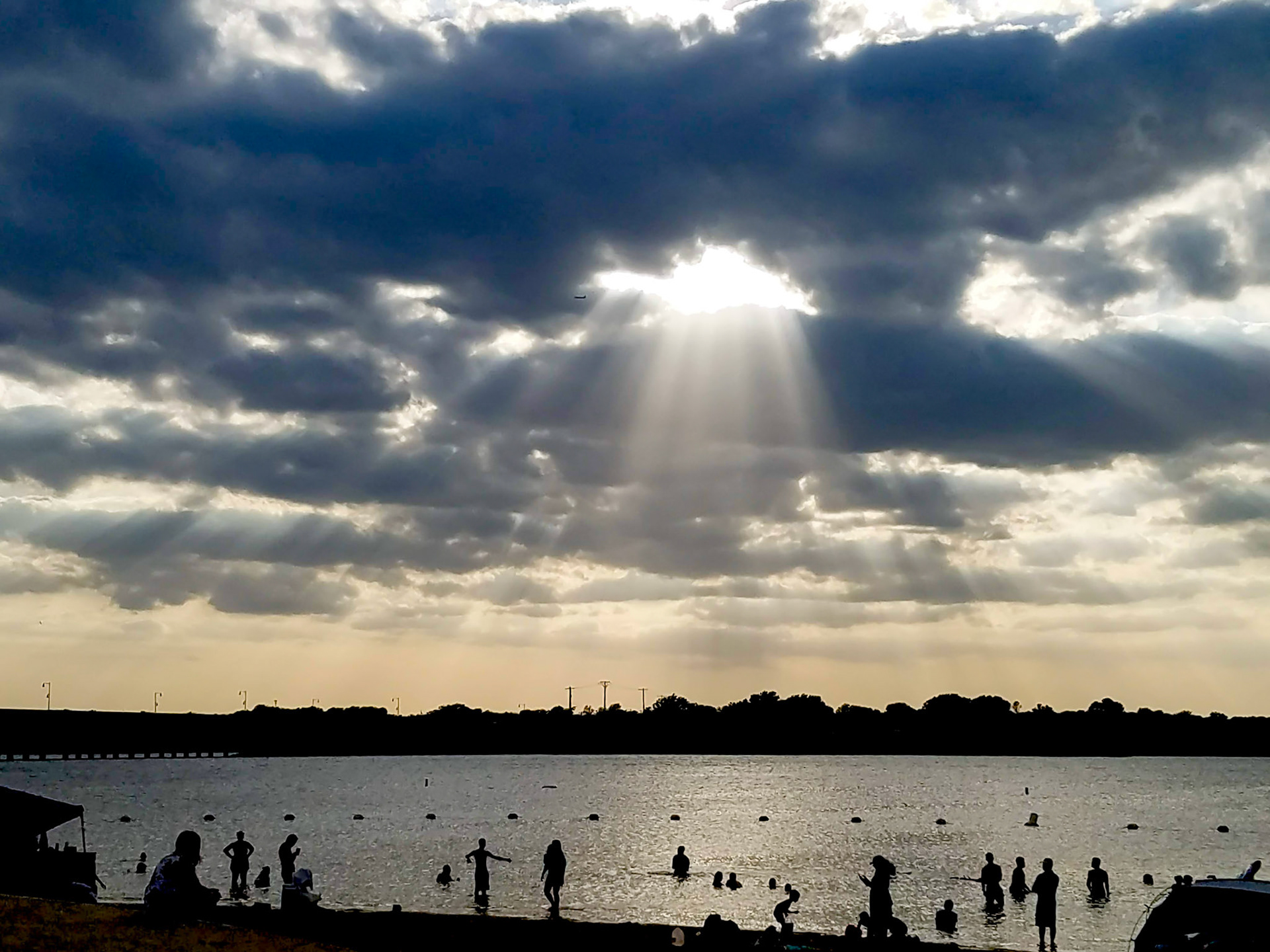 Lewisville, TX, US - Jun 23, 2018: Sun shining through gray clouds over beach and lake