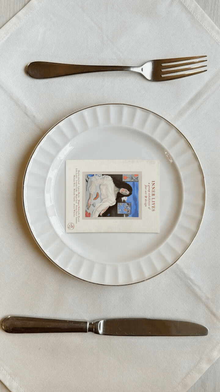 A white plate set on a linen napkin holds the exhibition invitation for Inner Lives at Salon 21, styled like a place setting with fork and knife — a poetic ‘invitation served’ concept. conceptual campaign image by Laurence Fugère for the surrealist design and art show in New York City.
