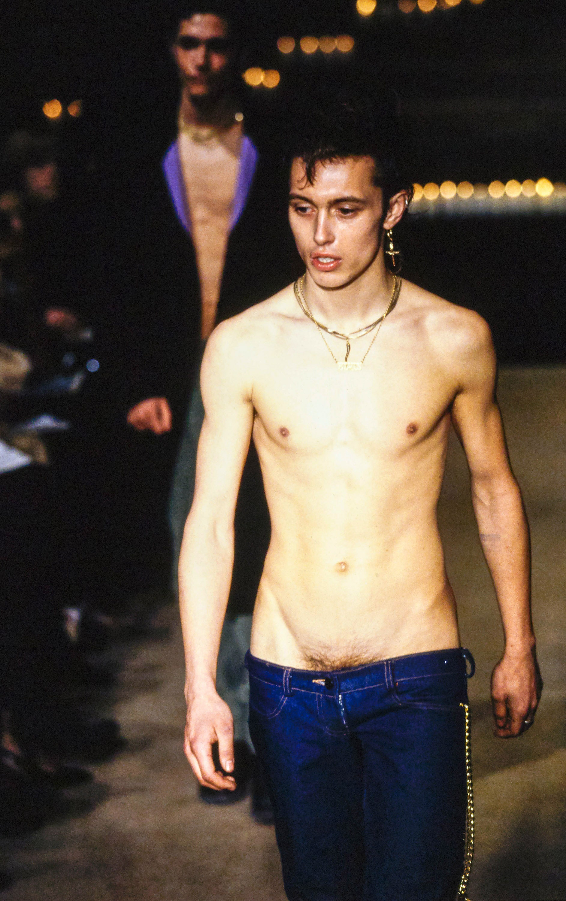 Shirtless male model walks the runway in ultra low-rise blue bumster jeans from Alexander McQueen’s 1996 “Dante” collection, highlighting the redefined human silhouette.
